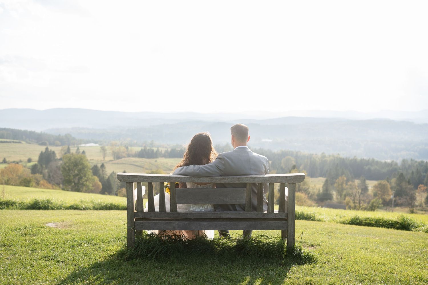 Couple sitting together on a wooden bench overlooking a scenic valley landscape.