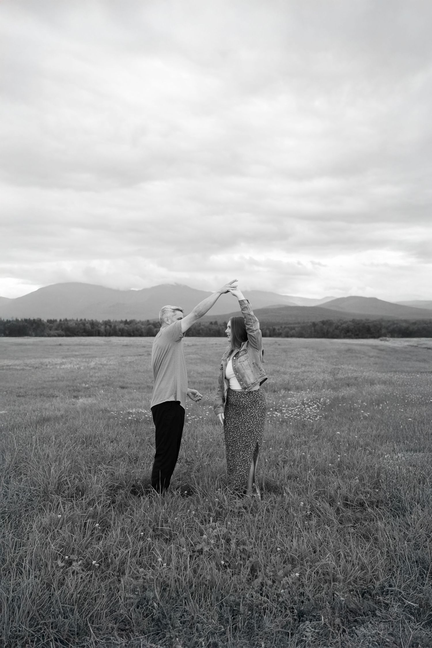 Black and white photo of couple dancing in open field with mountain views.