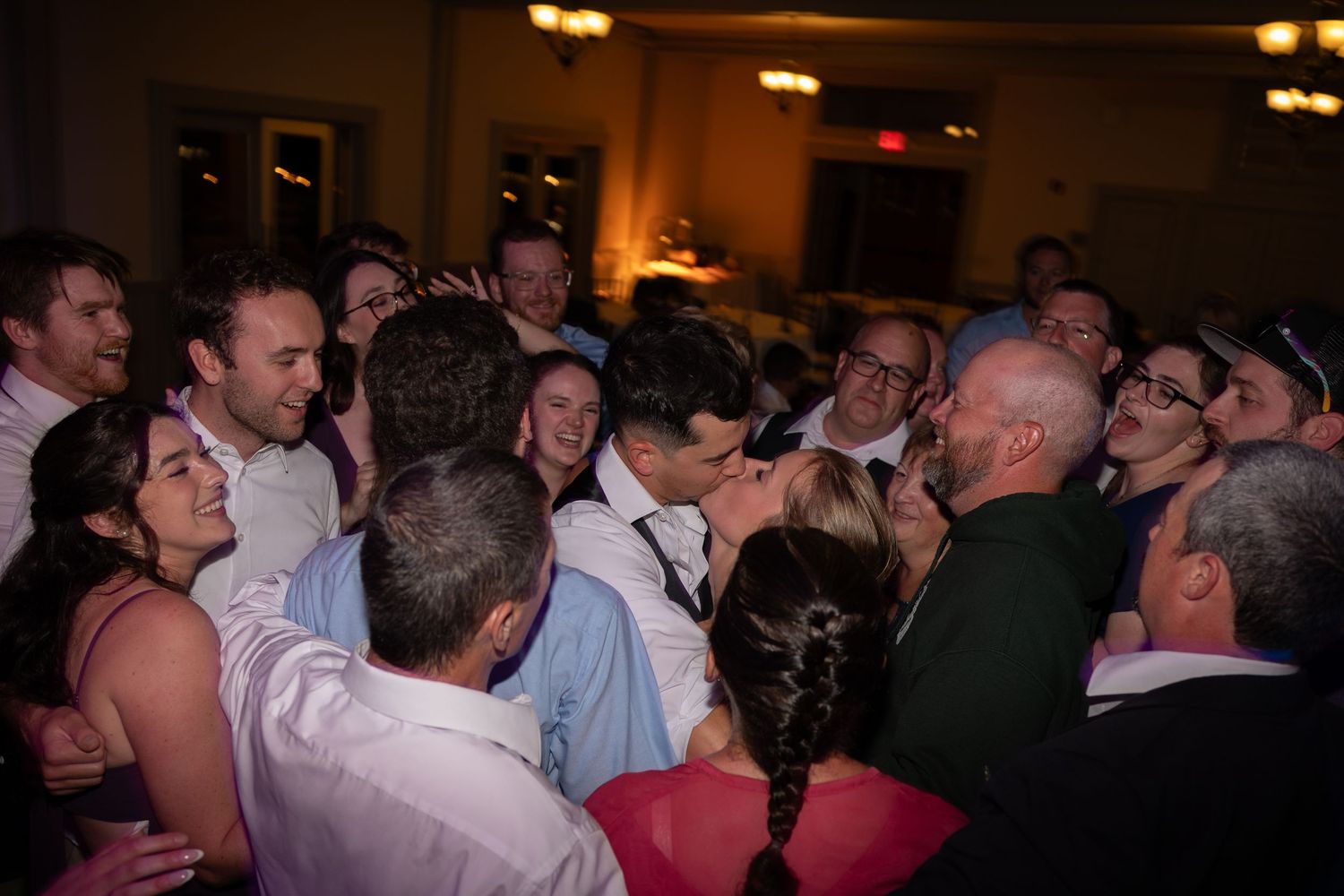 Joyful wedding reception guests crowding together on dance floor in candid celebration moment.