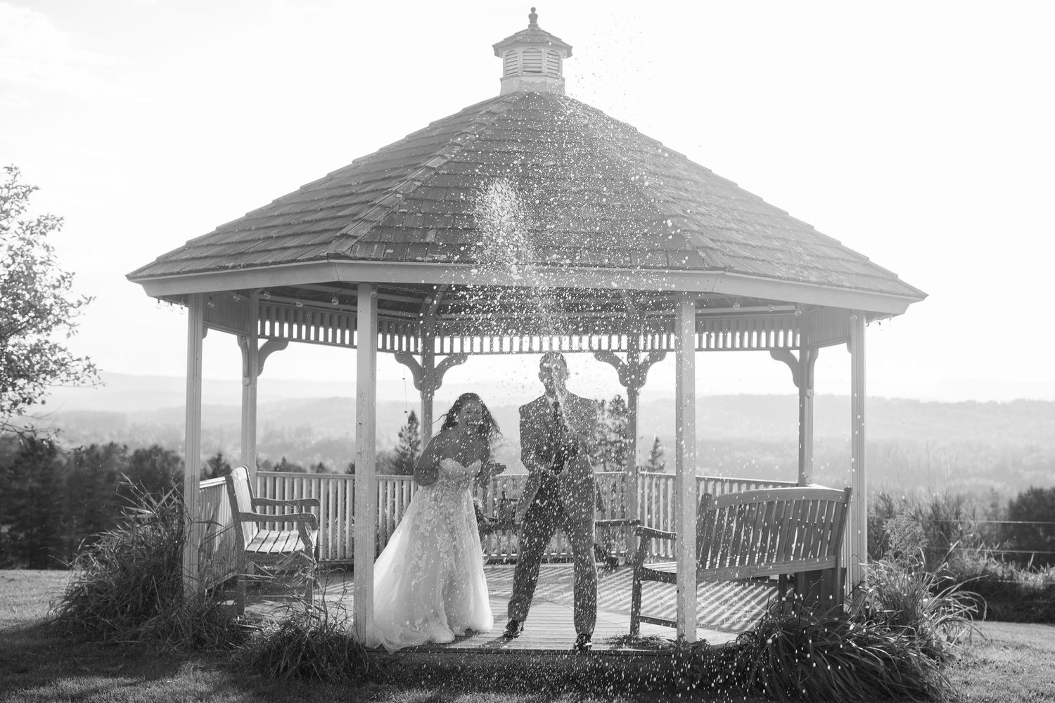 Black and white photo of bride and groom celebrating under a gazebo with confetti.