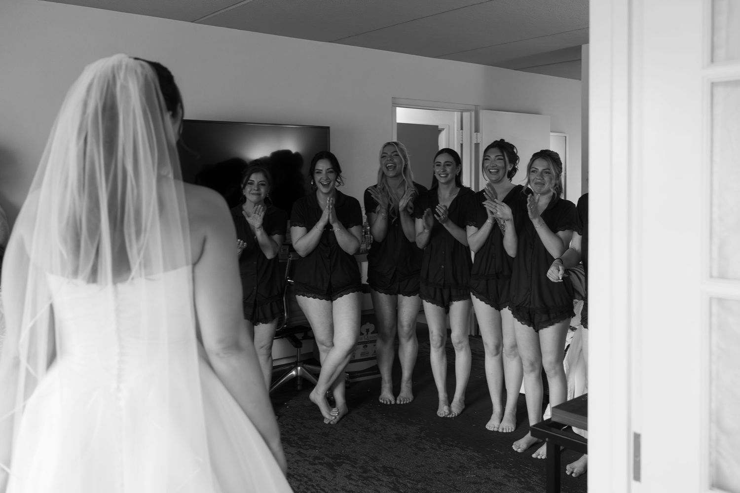 Black and white photo of bridesmaids reacting with joy seeing bride in wedding dress for first time.