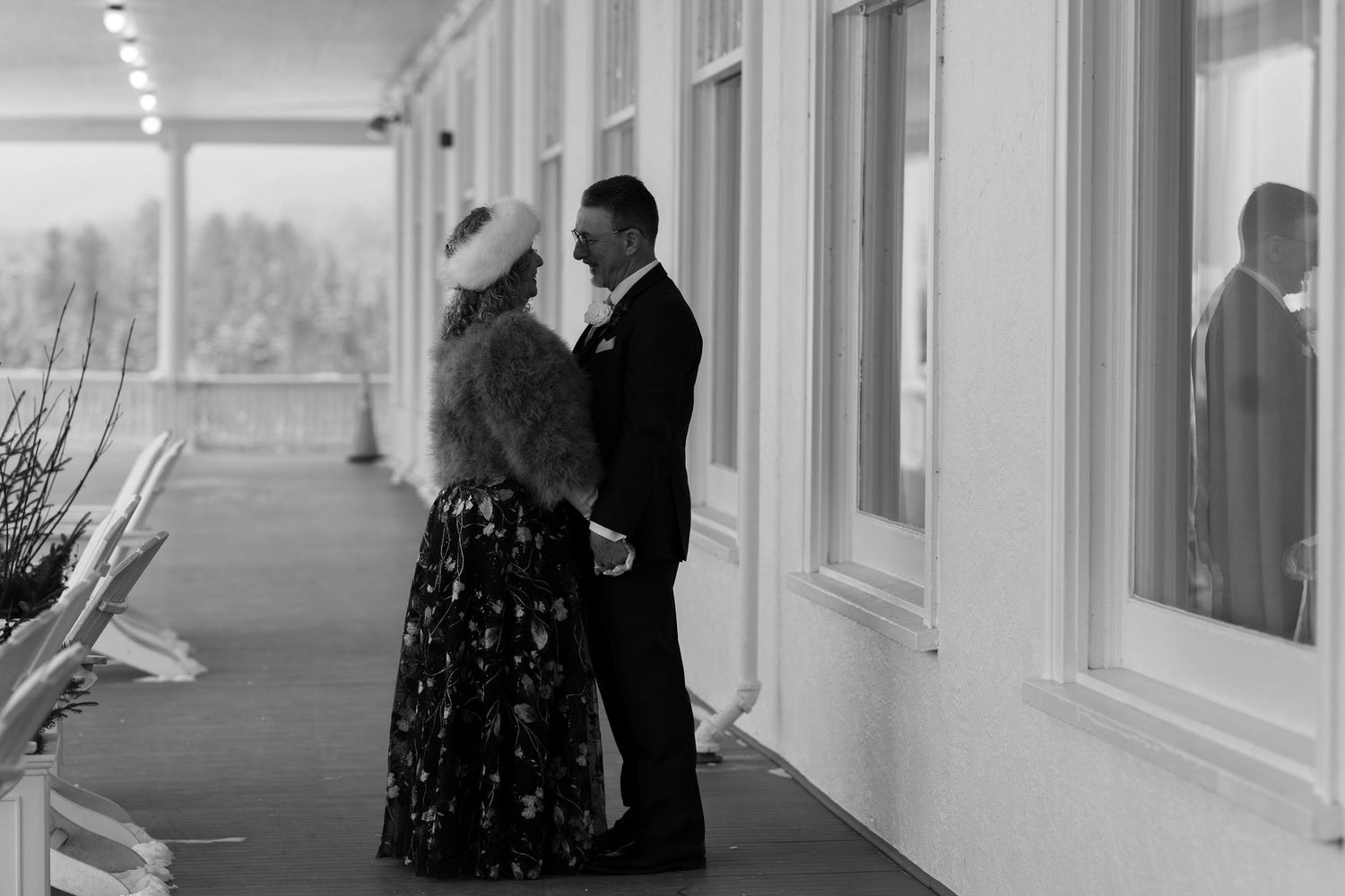 Black and white photo of bride and groom holding hands on a hotel veranda.