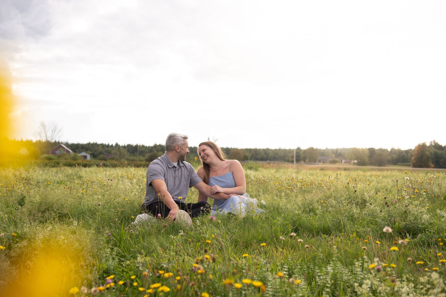 A couple sits together in a sunny wildflower meadow at golden hour.