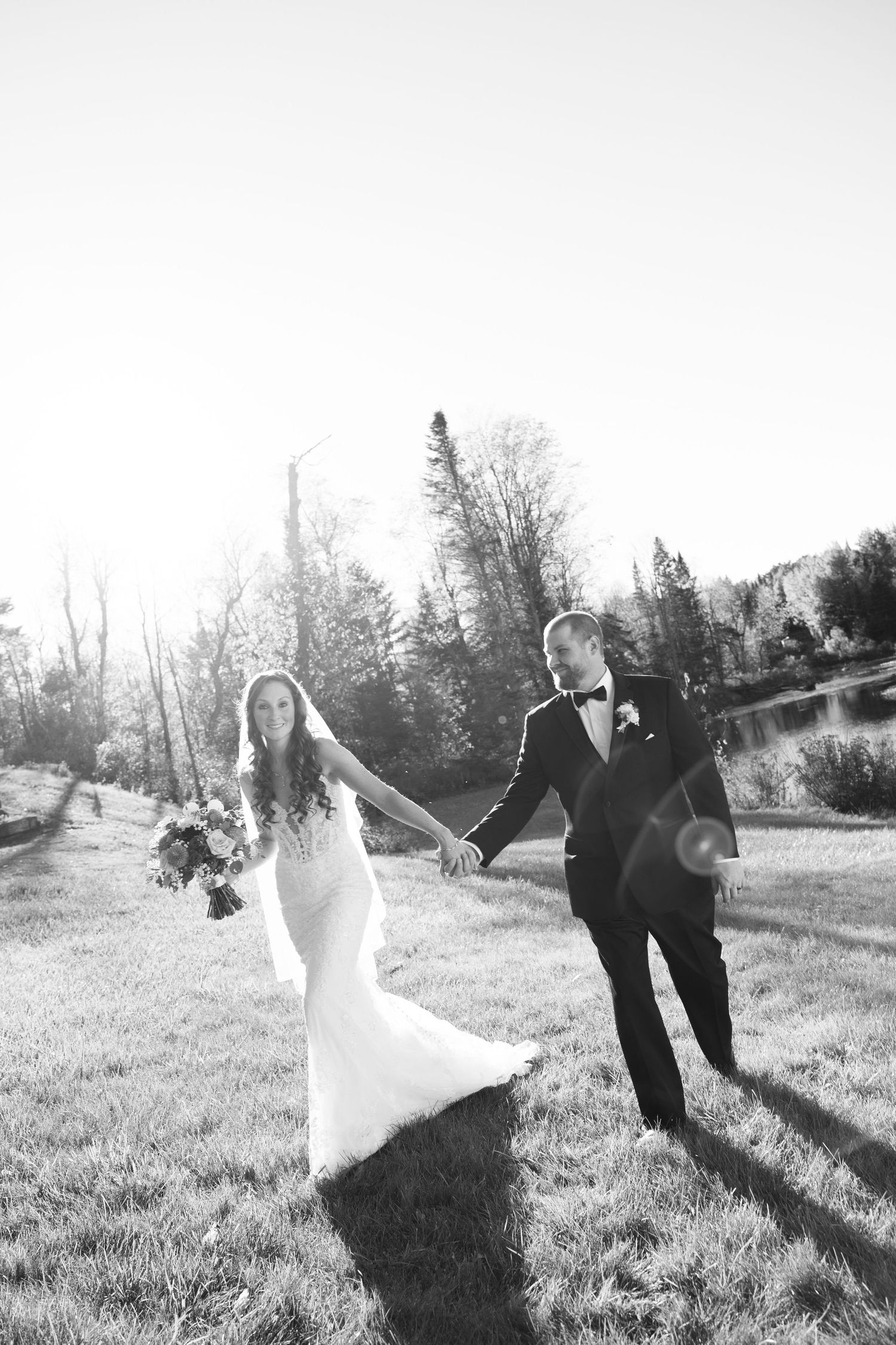 Black and white photo of a bride and groom holding hands walking through a grassy field on their wedding day.