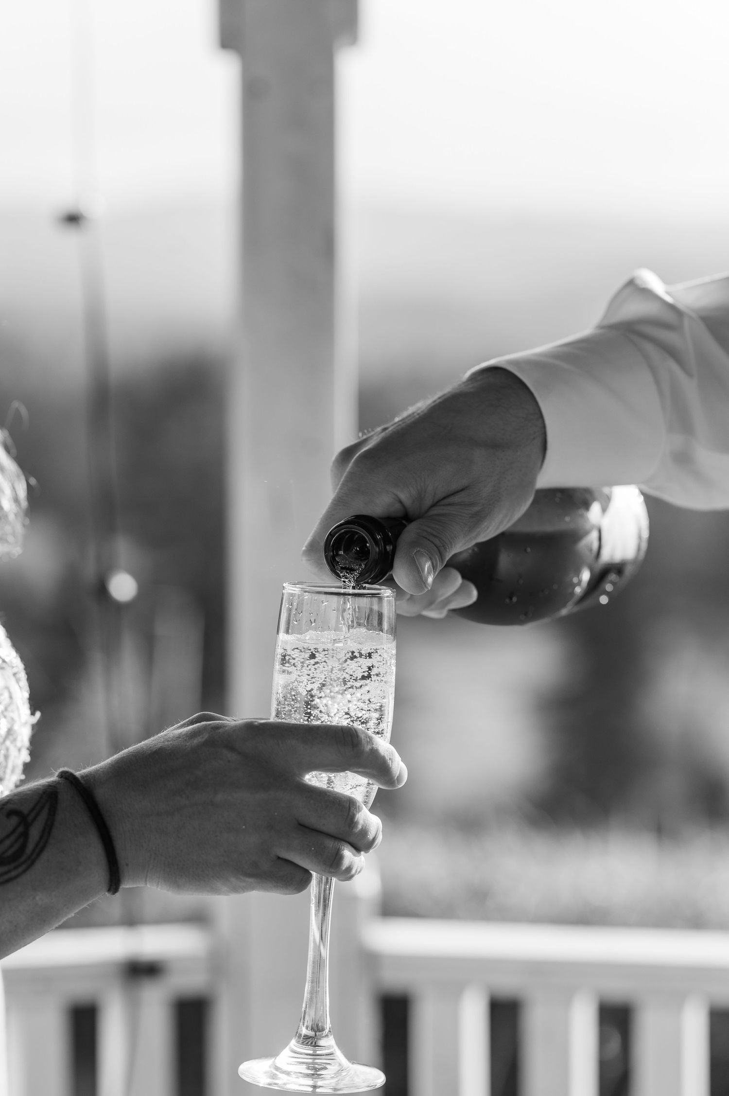 Black and white close-up of champagne being poured into a flute at an outdoor wedding celebration.
