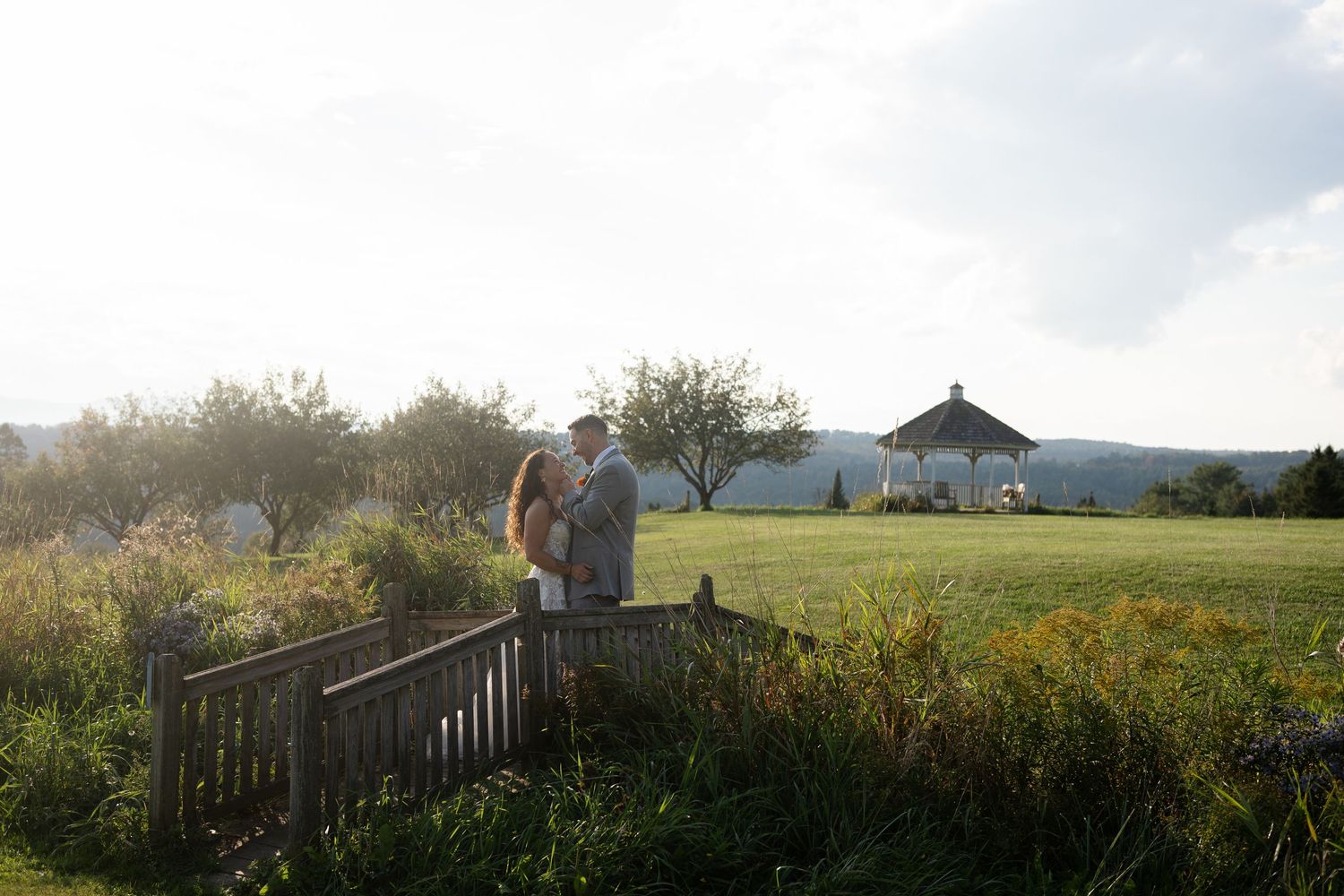 Couple standing on a wooden bridge surrounded by lush greenery at golden hour.