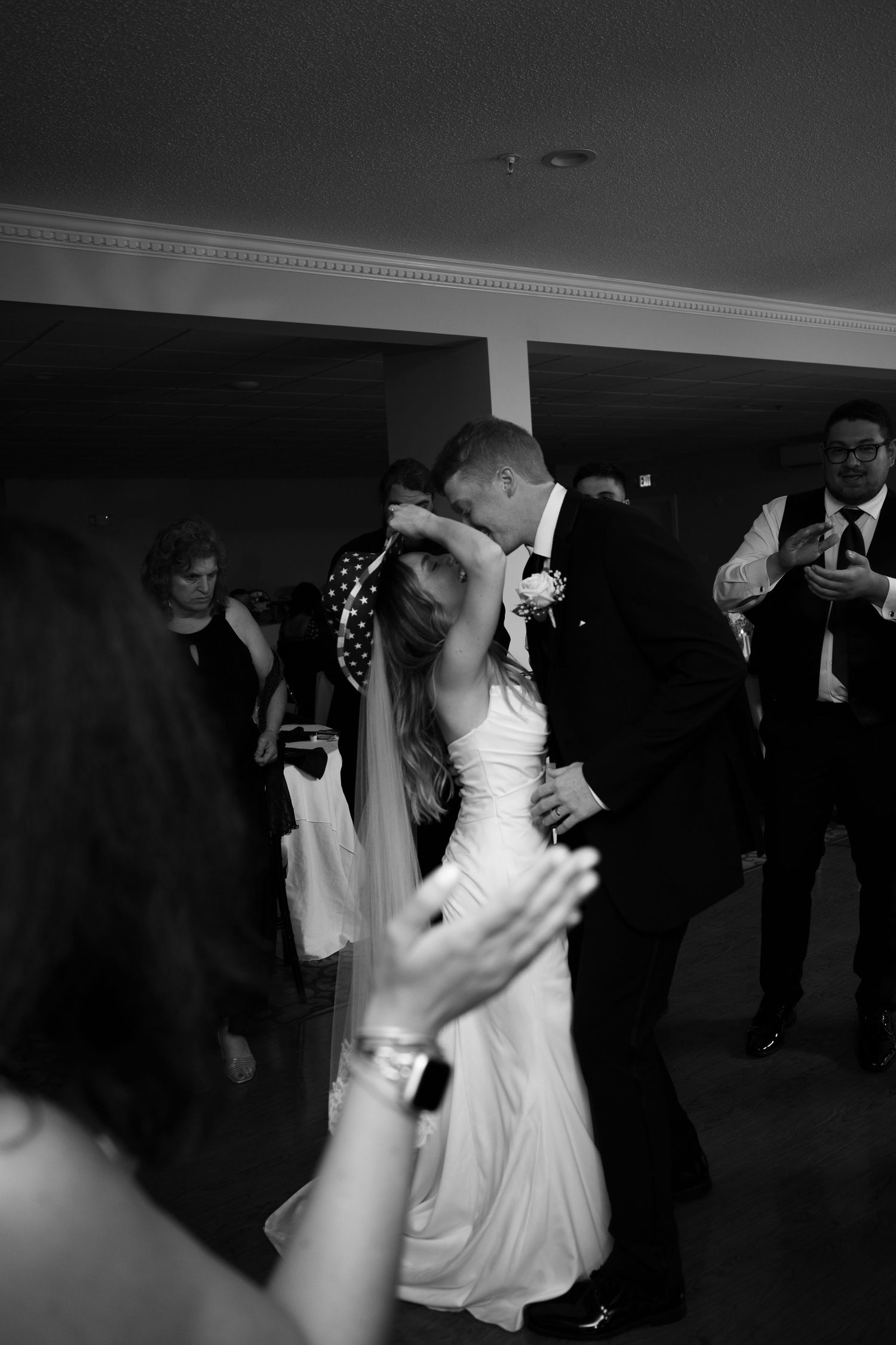 Black and white photo of bride and groom sharing first dance kiss at wedding reception.