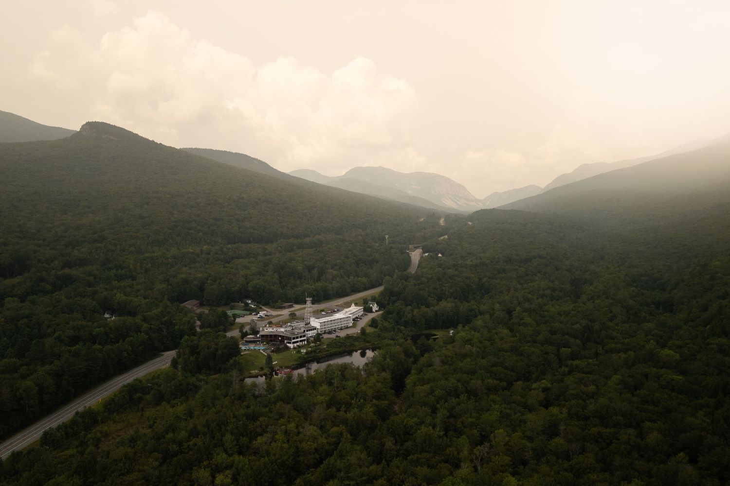 Aerial view of white building nestled in misty mountain valley surrounded by dense green forest.