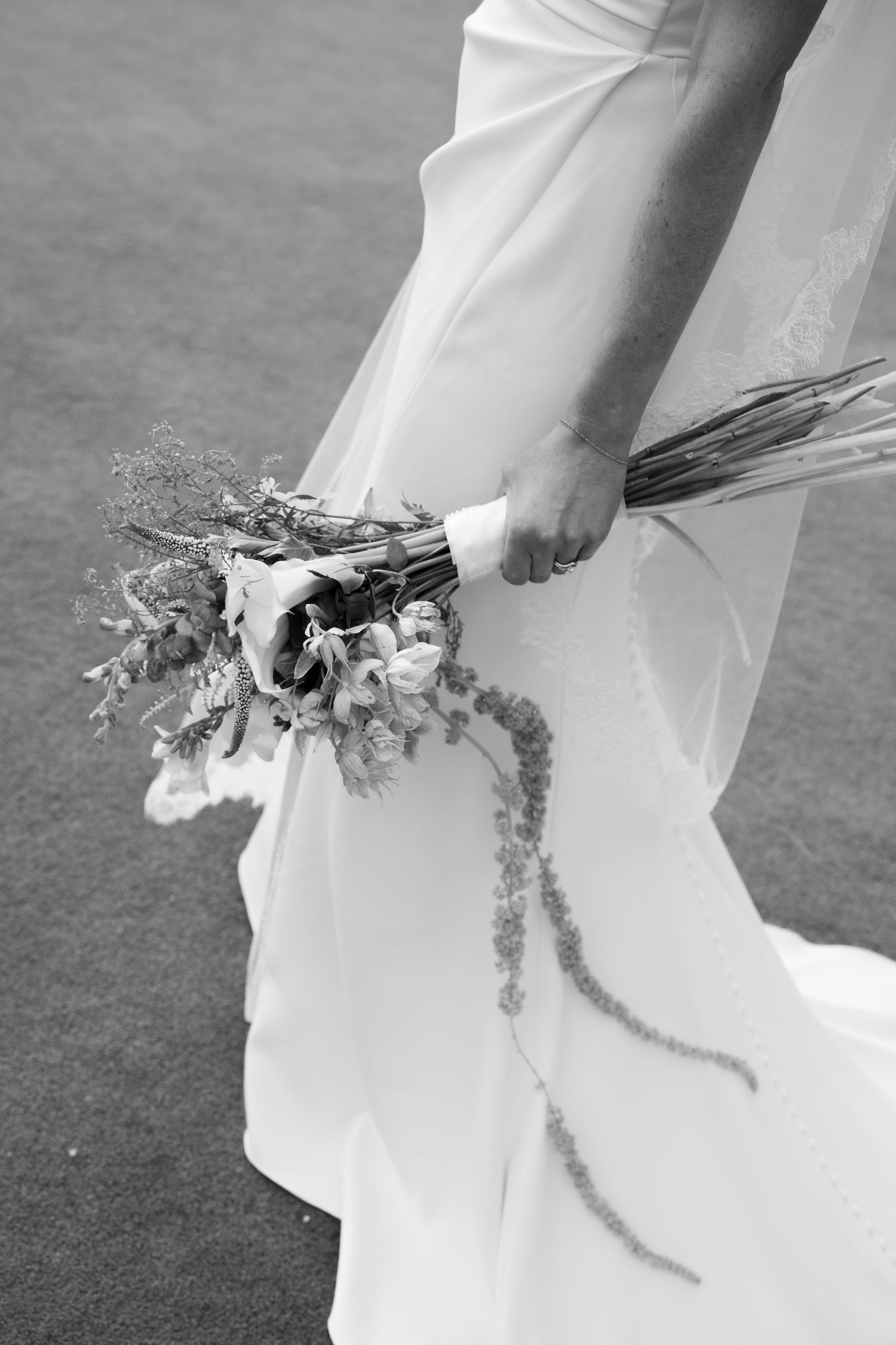Black and white photo of a bride holding a wildflower bouquet in her wedding dress.