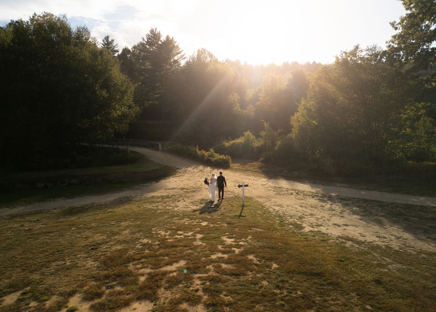 Aerial view of wedding couple with photographer at golden hour in a sunlit forest clearing.
