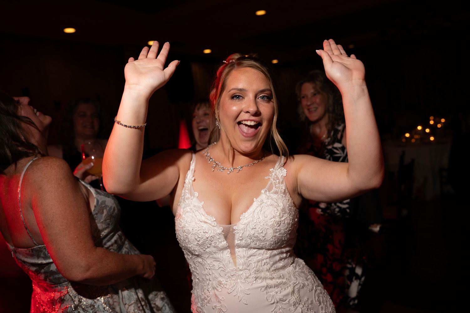 Joyful bride in white lace gown dancing with arms raised at wedding reception celebration.