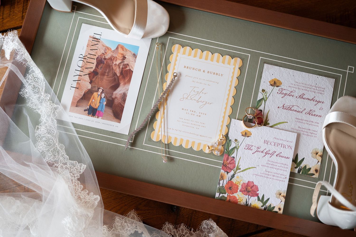 Elegant wedding invitation suite with floral designs, scalloped edges, and bridal accessories on a wooden tray.