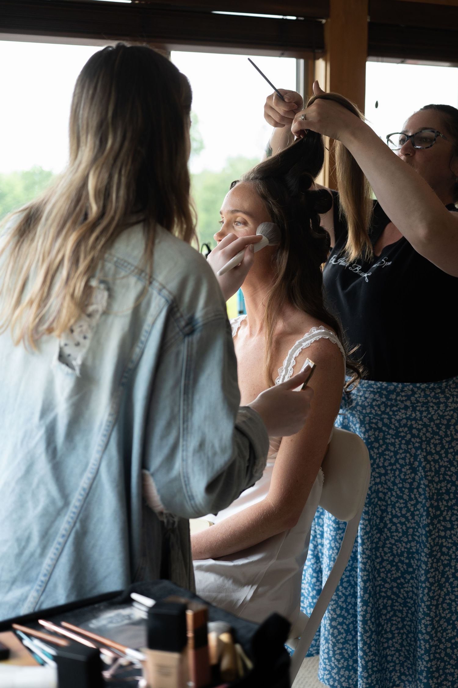 Bride getting hair and makeup done by two stylists before her wedding ceremony.