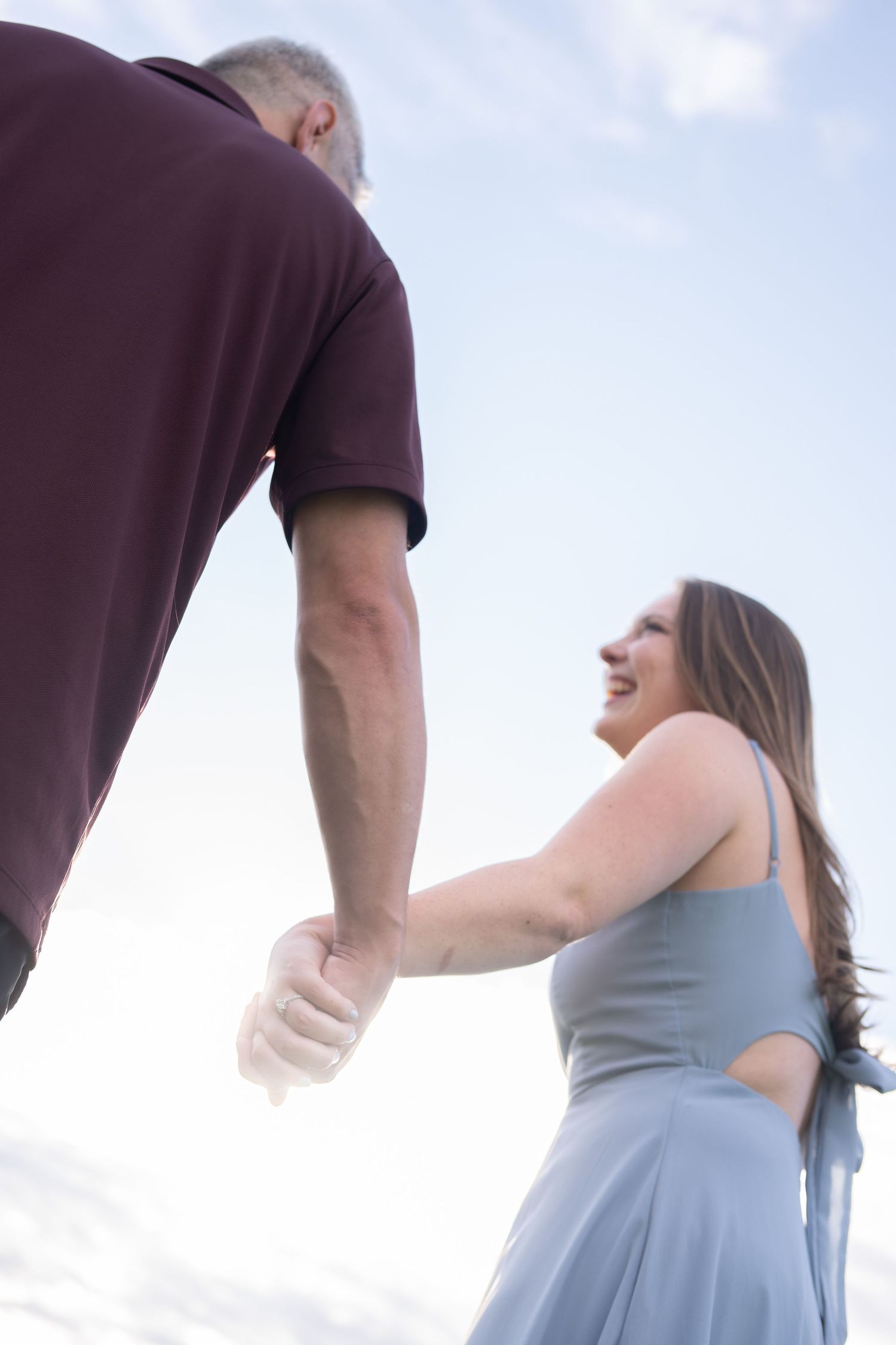A woman laughs joyfully while holding hands with a man outdoors.
