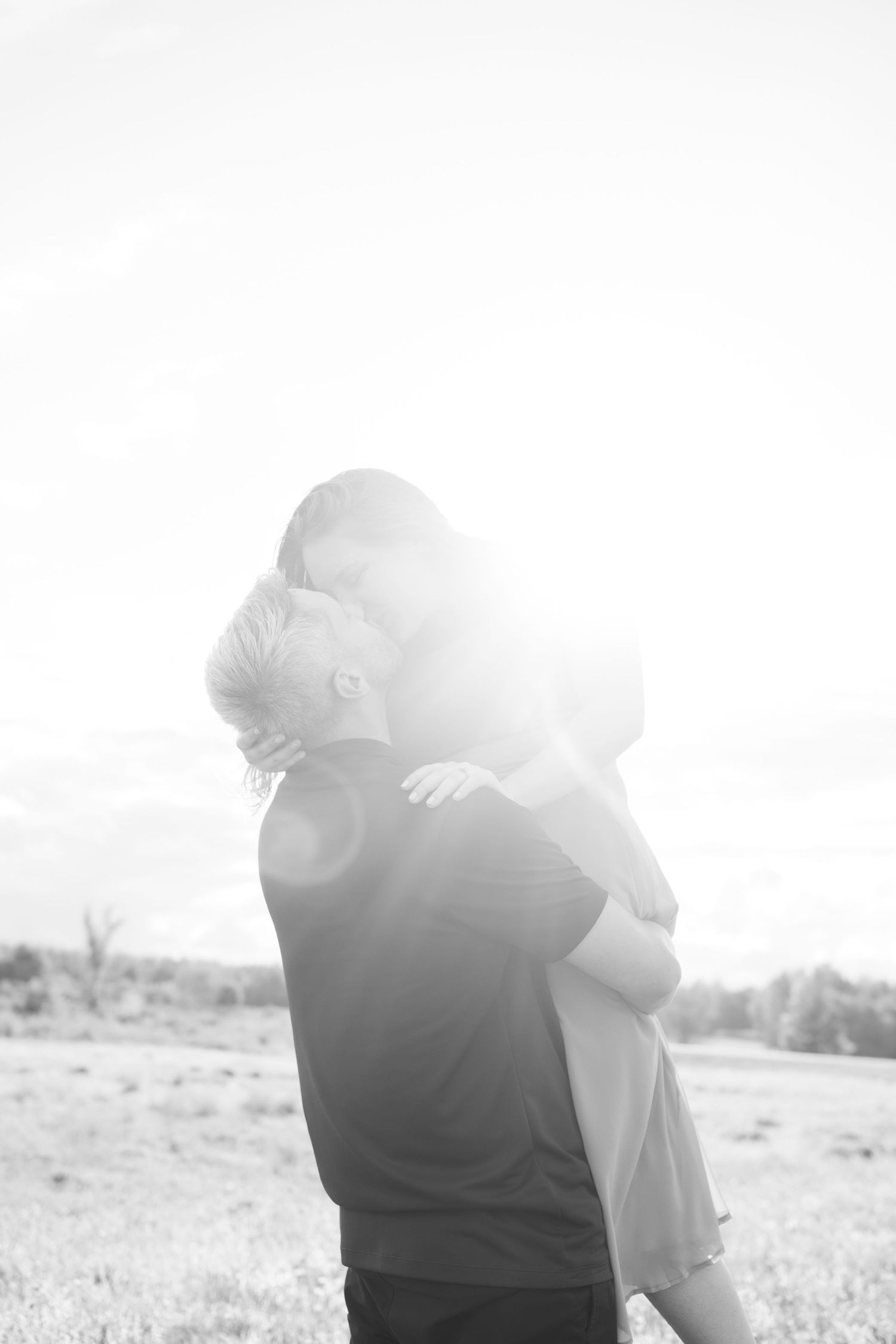 Black and white backlit photo of couple embracing in bright sunlight outdoors.