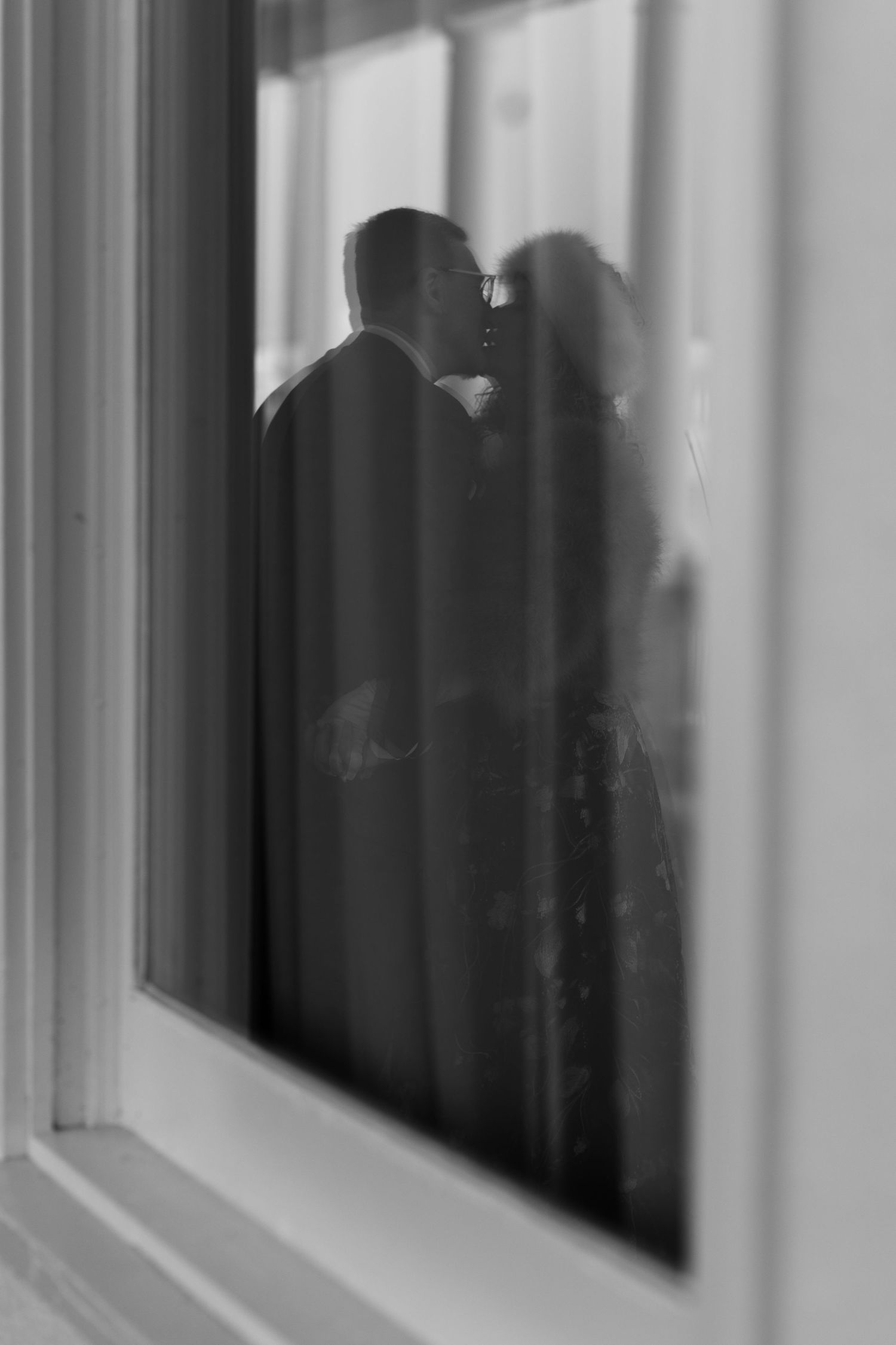 Black and white silhouette of couple kissing seen through a window reflection.