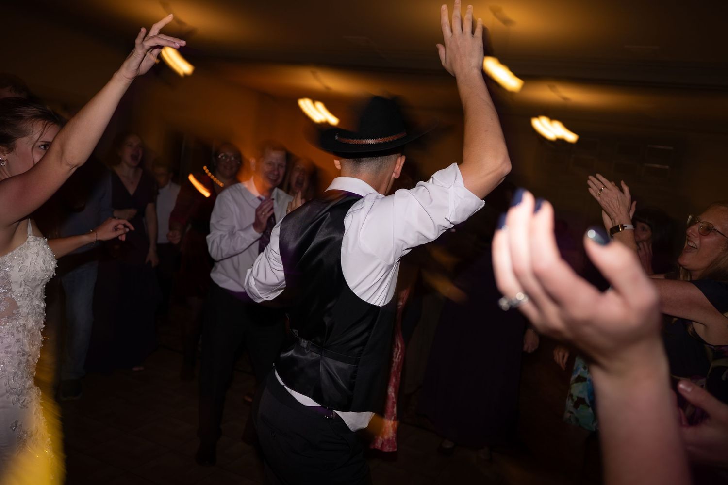 Energetic wedding reception dance floor scene with guests celebrating under warm ambient lighting.