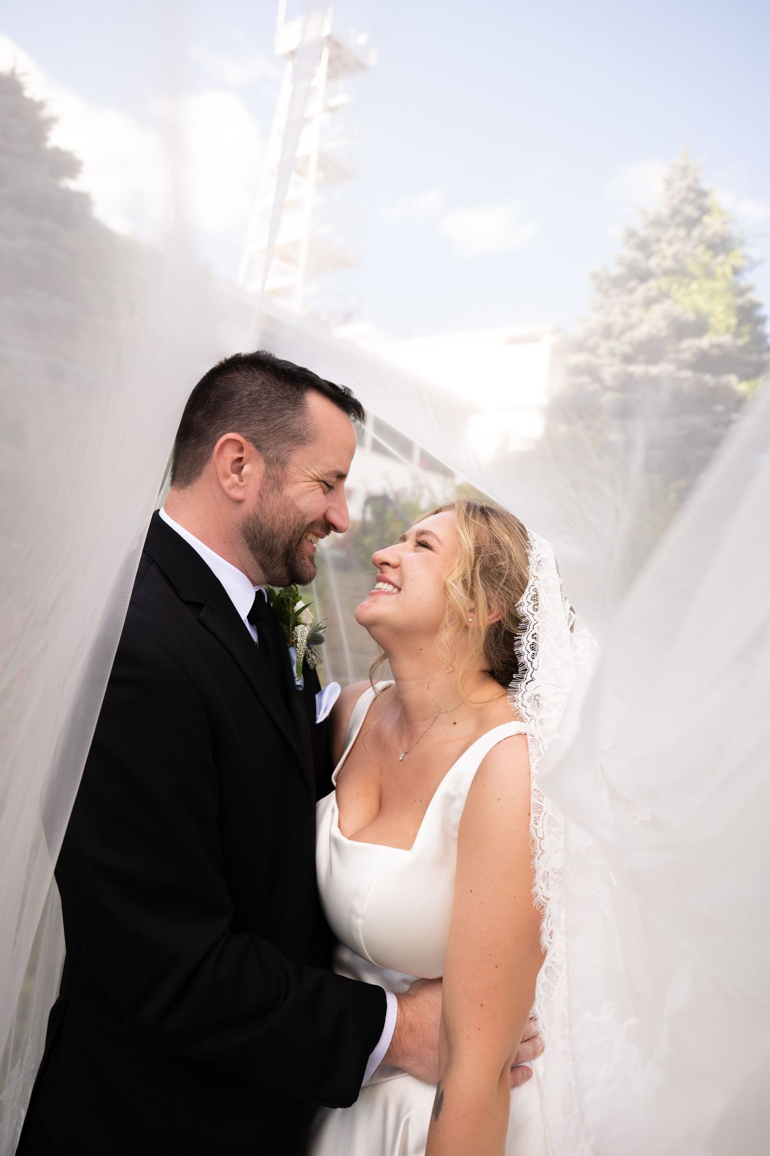 A joyful bride and groom share a romantic moment wrapped in a flowing veil on their wedding day.