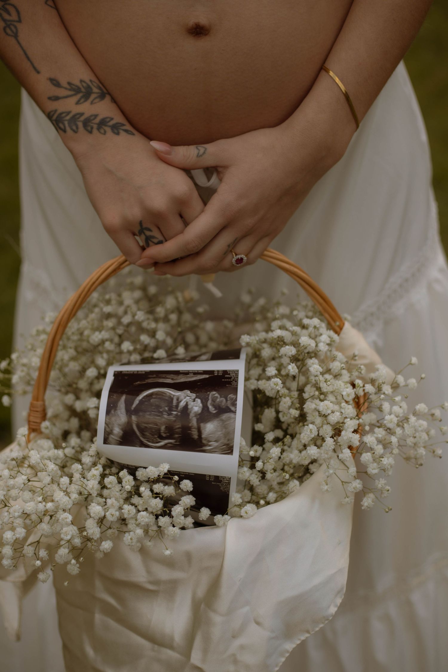 Pregnant woman in white dress holding a wicker basket with baby's breath flowers and an ultrasound photo.