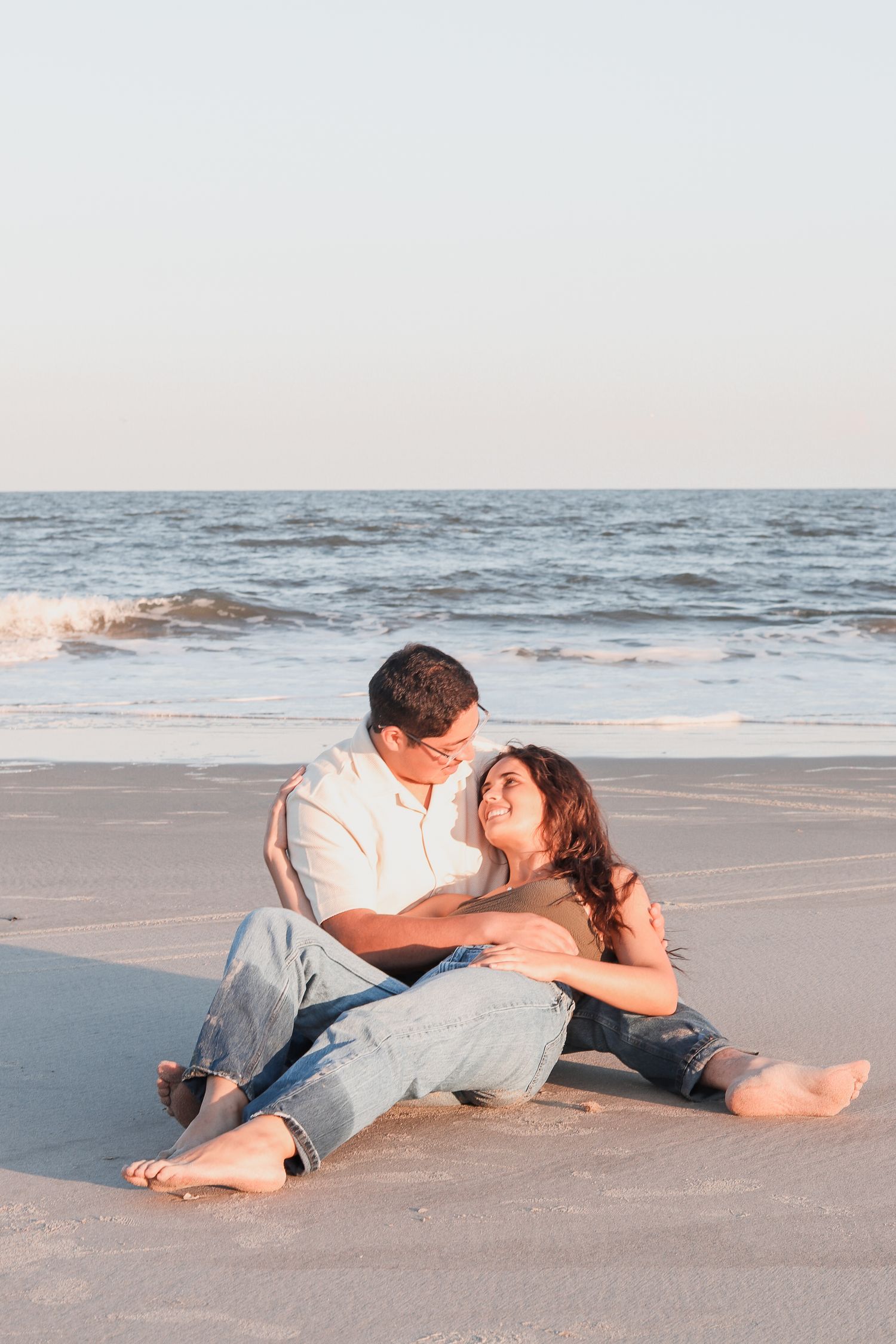 Romantic couple lying together on a sandy beach at sunset.