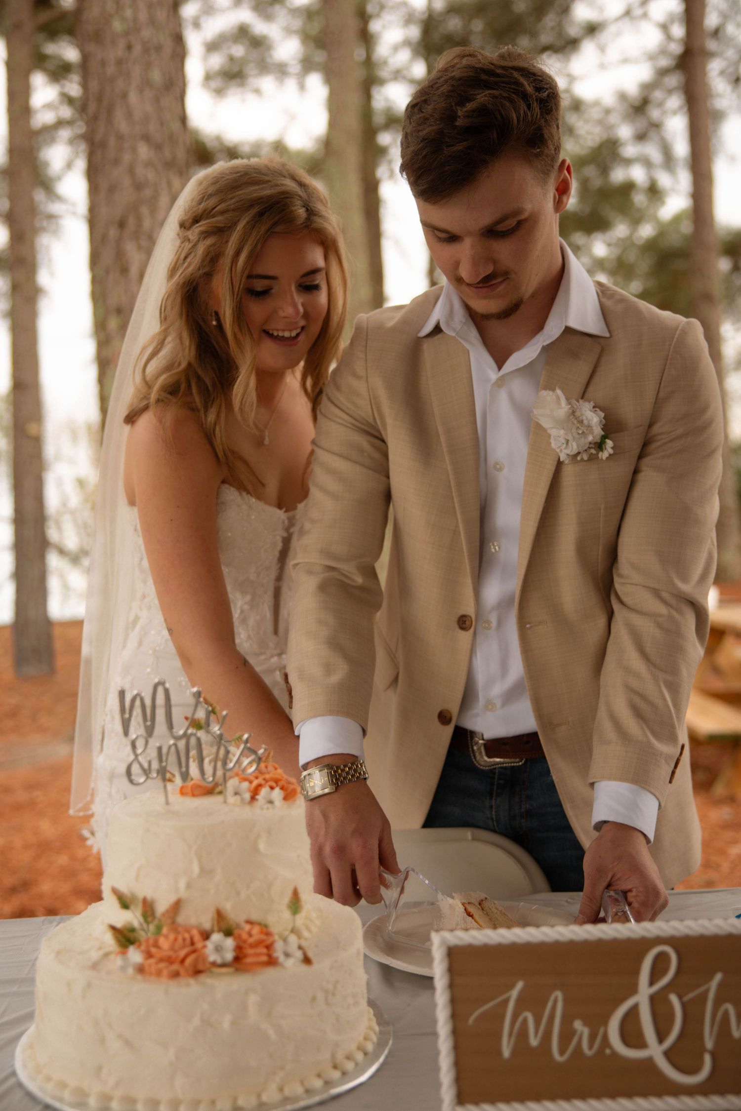 Bride and groom cutting their white wedding cake outdoors, decorated with orange flowers and a Mr. & Mrs. topper.