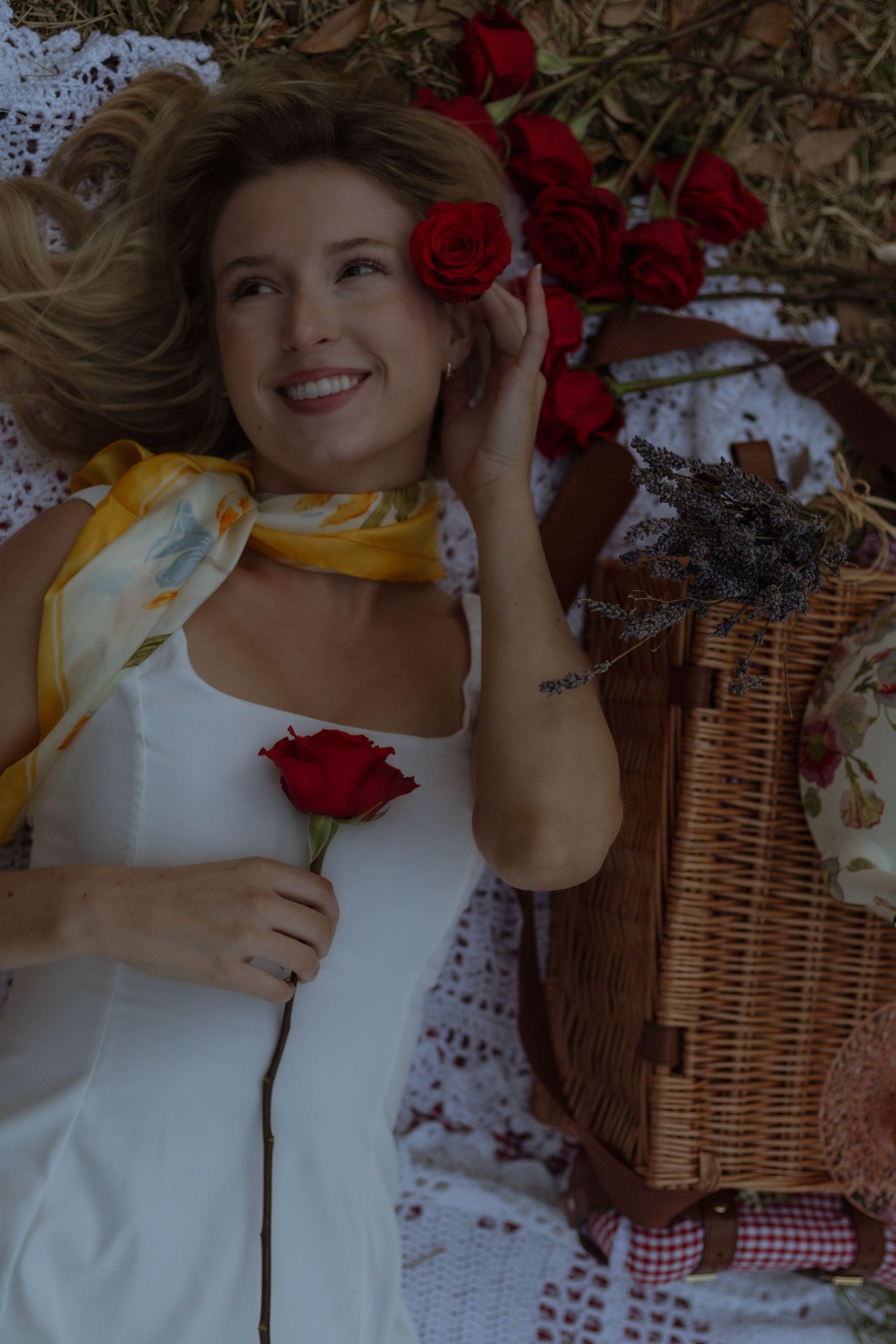A picnic scene with red roses, a wicker basket, and white dress against a floral backdrop.