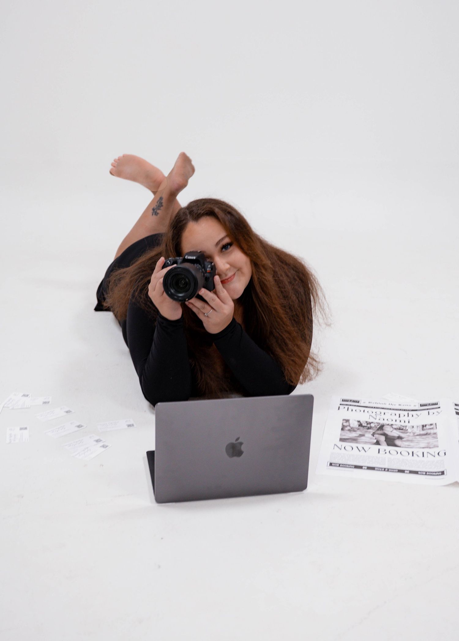 Creative photographer lying on floor with laptop and camera during studio photoshoot.