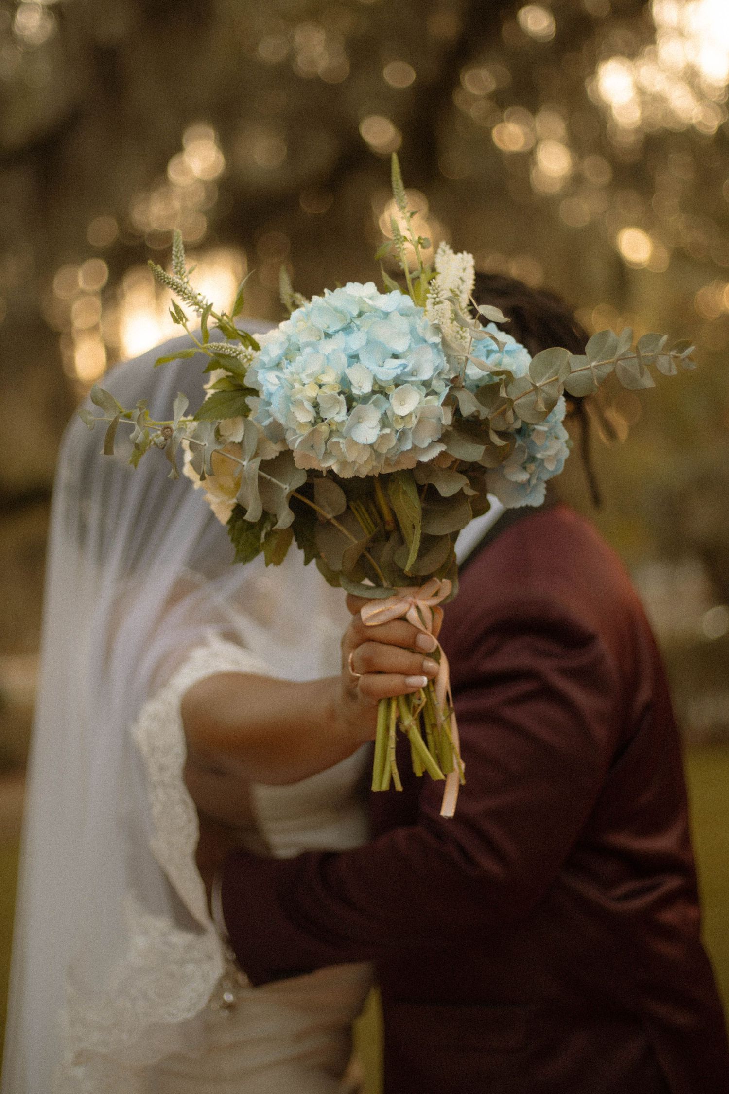 A beautiful white hydrangea wedding bouquet held up against a warm bokeh background during a romantic ceremony.