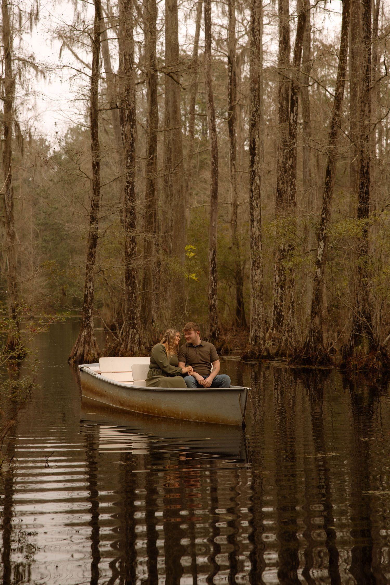 Couple sitting close together in a small boat surrounded by cypress trees in a misty swamp.