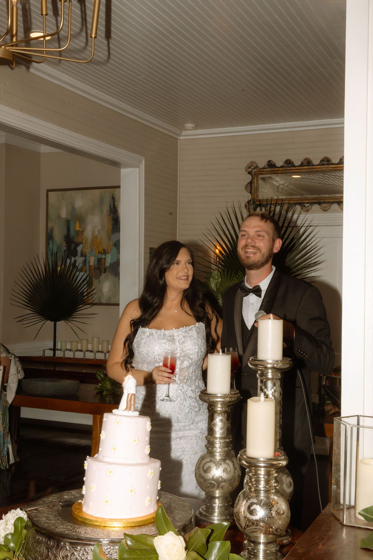 Bride and groom smiling beside a white wedding cake with candles at their elegant indoor reception.