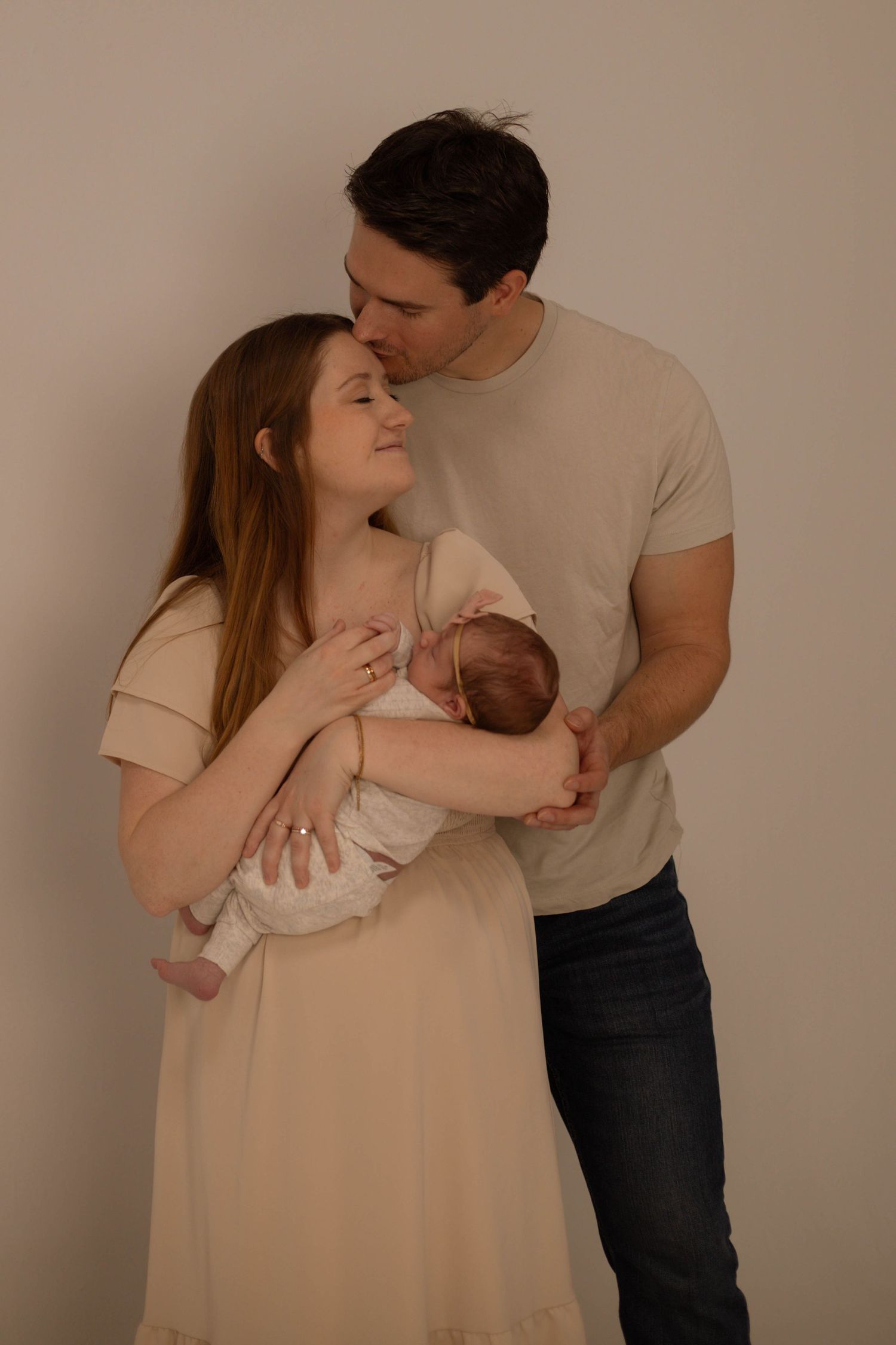A couple tenderly holds their newborn baby during a professional studio portrait session against a neutral background.