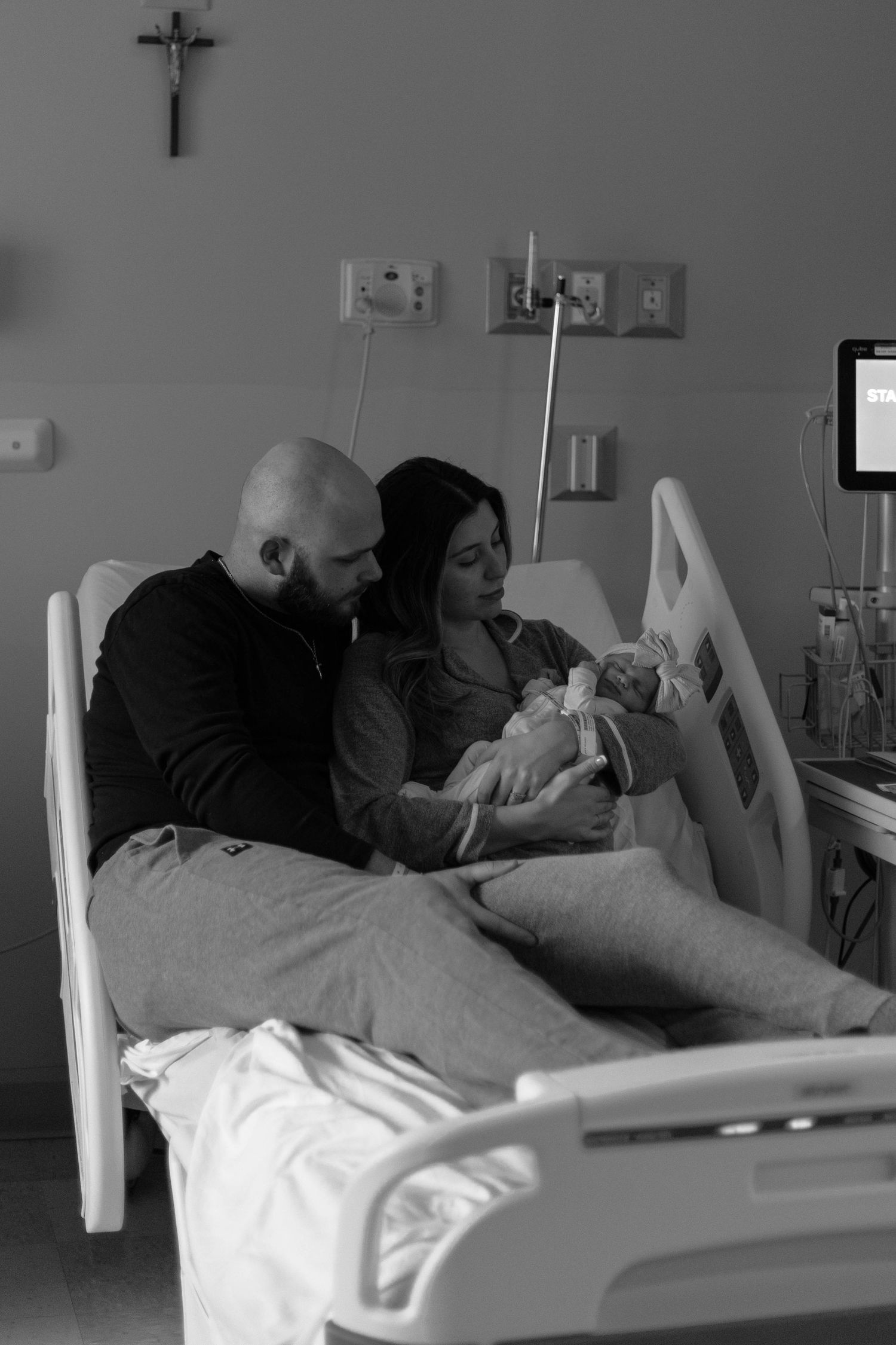 Black and white photo of new parents in hospital bed lovingly holding their newborn baby after delivery.