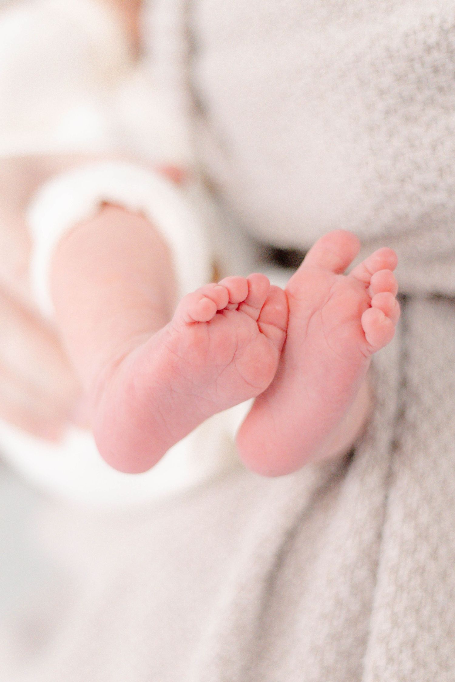 Tiny pink baby feet peek out from soft white blanket in tender newborn detail shot.