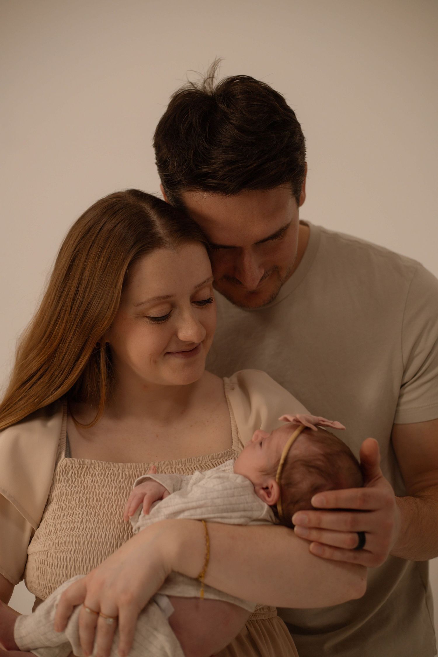 Young couple tenderly gazing at their sleeping newborn baby girl in a warm studio portrait.