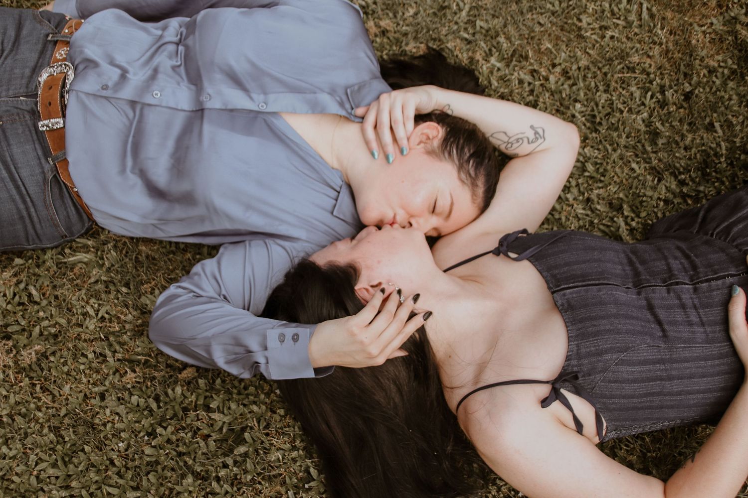 Couple sharing intimate moment while lying on grass outdoors.