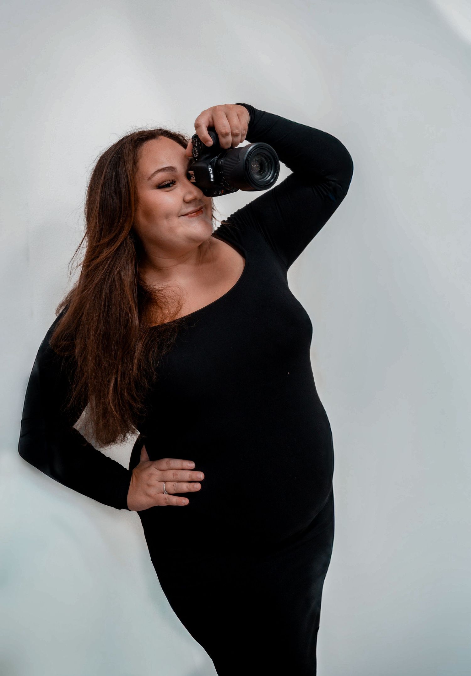 Creative self-portrait of photographer in black dress holding camera.