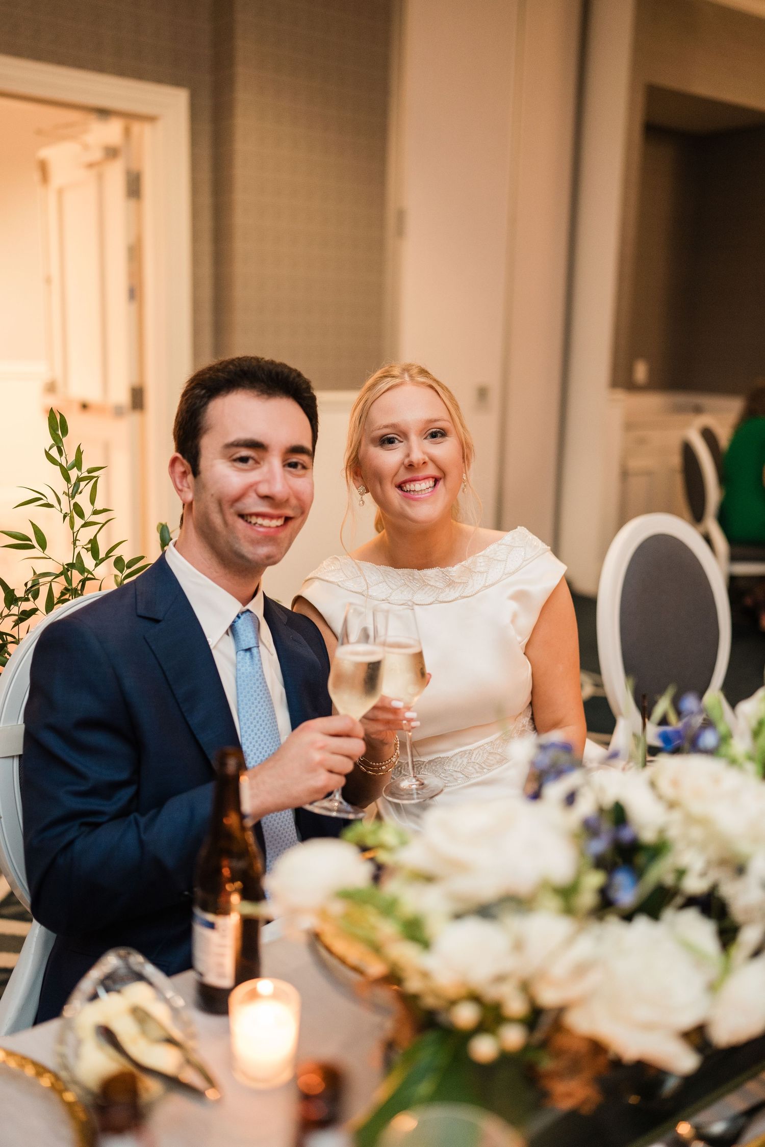 A couple shares a joyful moment at their wedding reception dinner table with floral centerpieces and candlelight.