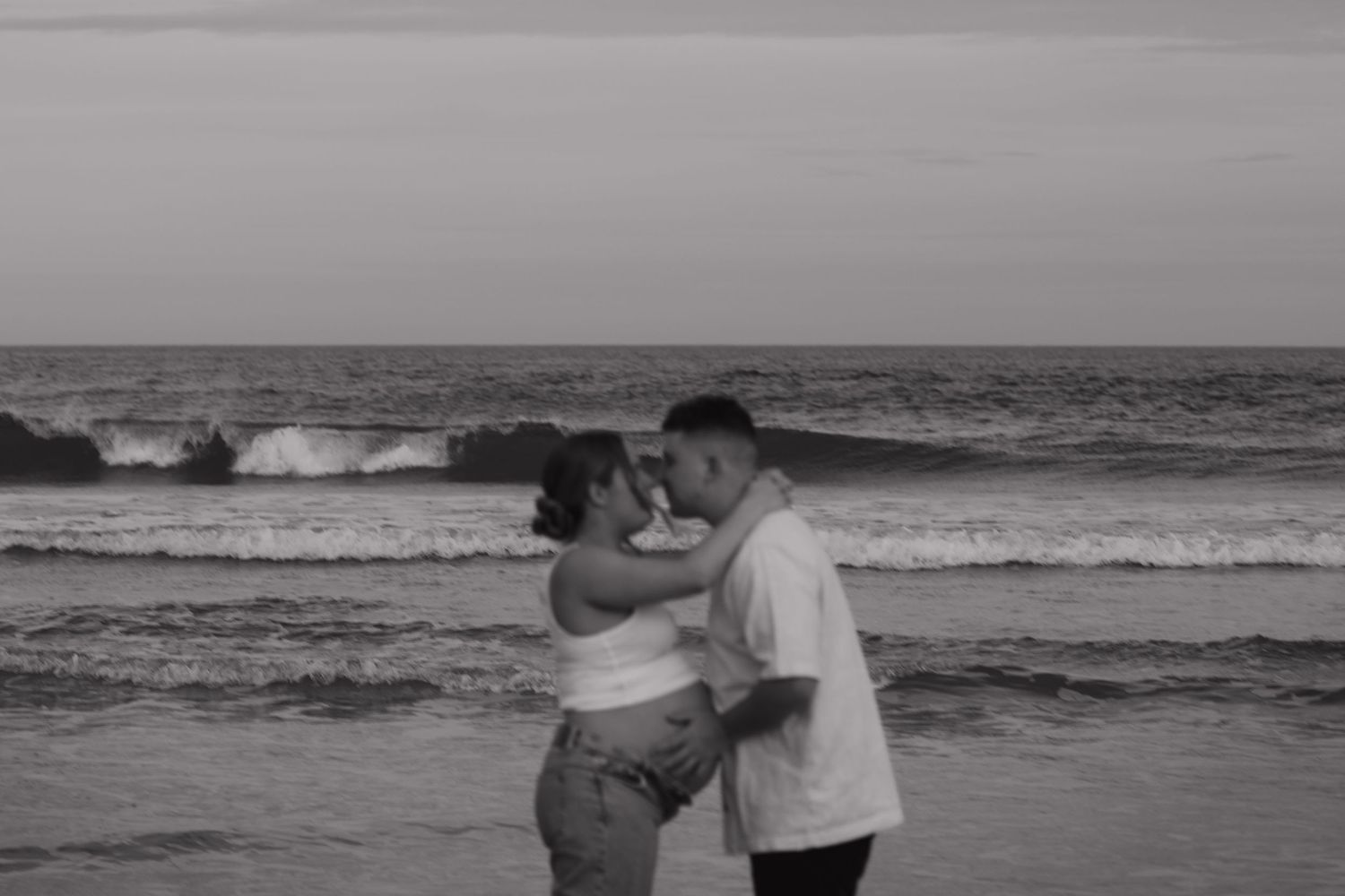 Couple embracing on beach with ocean waves in background at sunset.