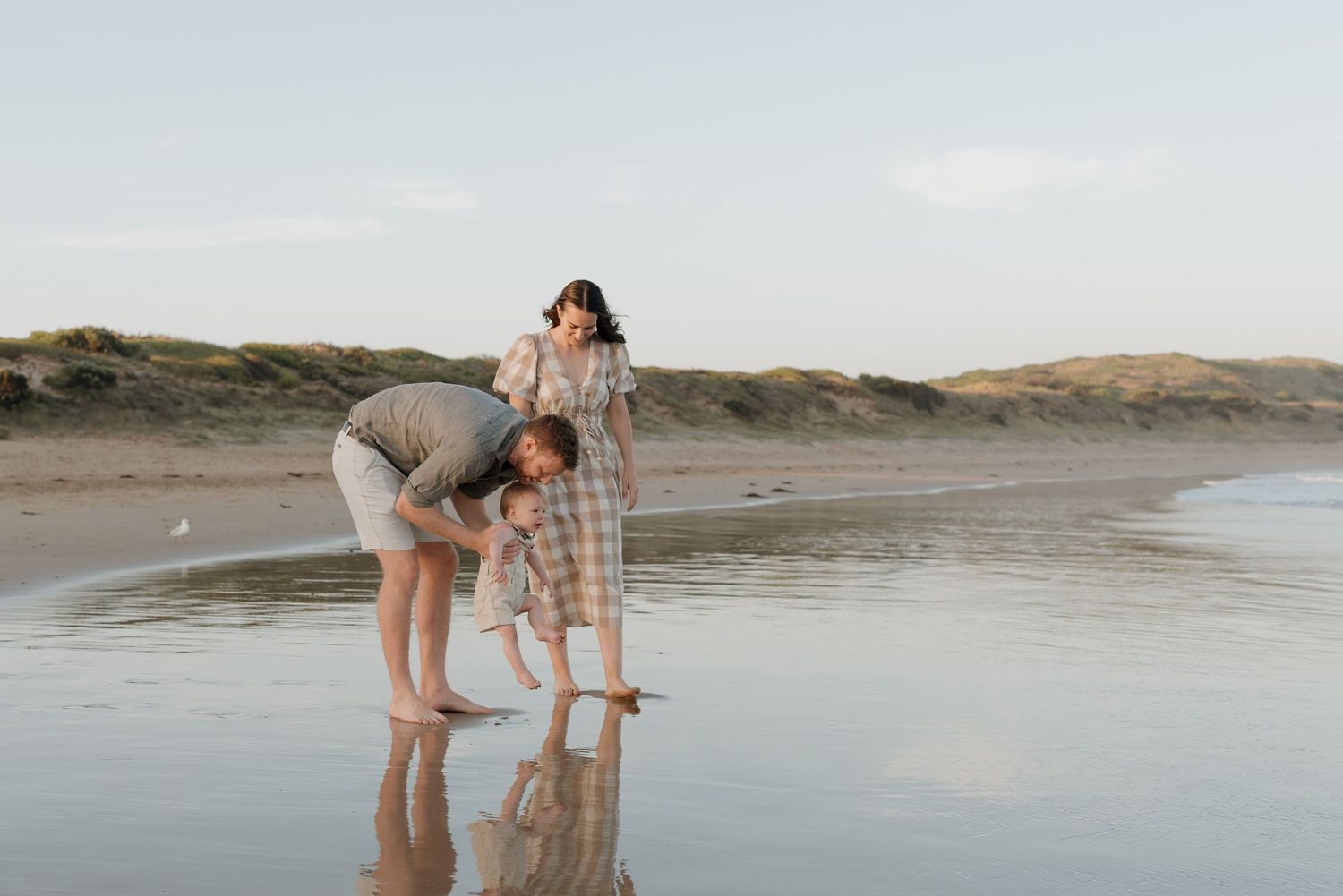 People enjoying a peaceful moment together on a serene beach at sunset with reflections in the wet sand.