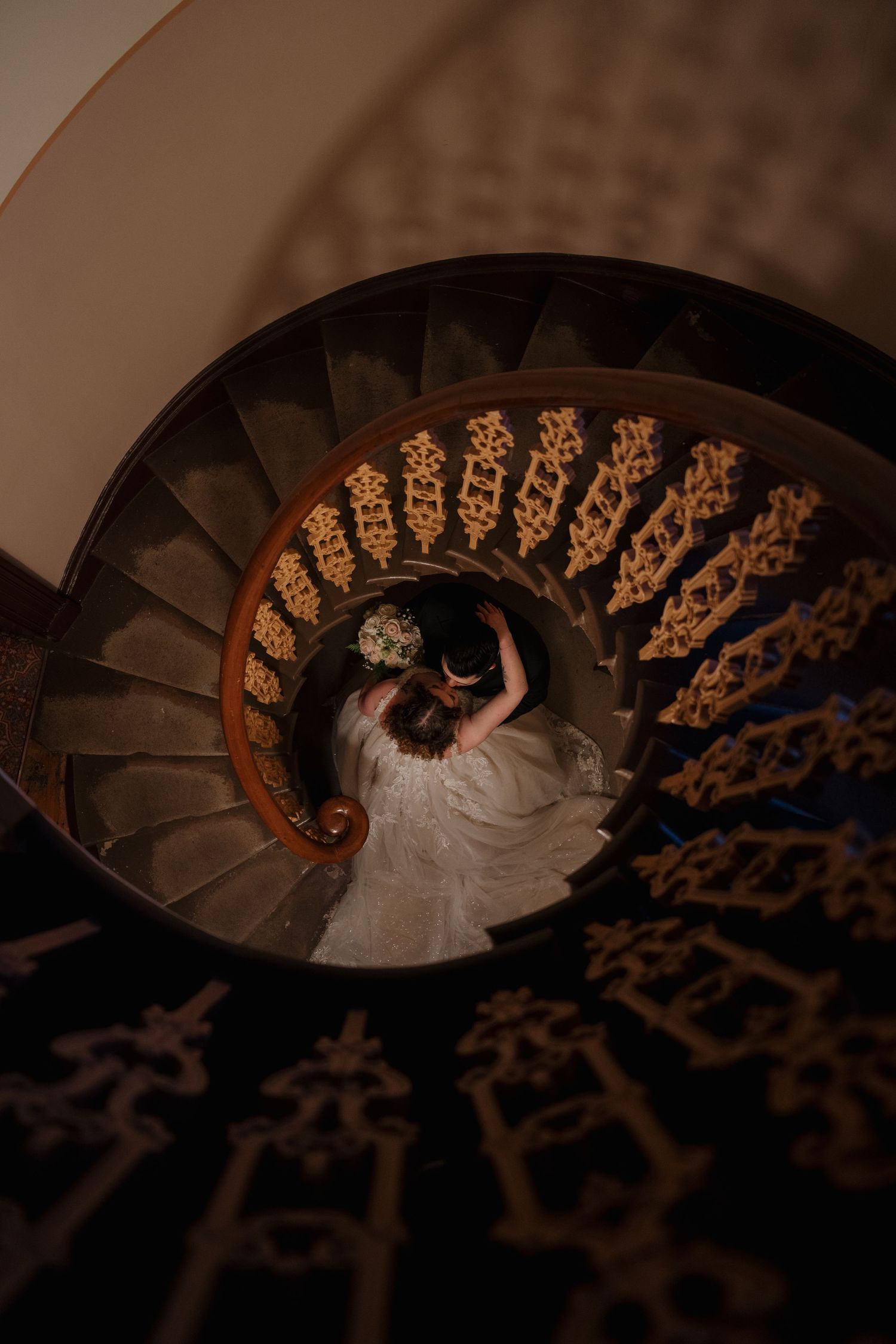 Aerial view of spiral staircase with ornate details and flowing white dress.