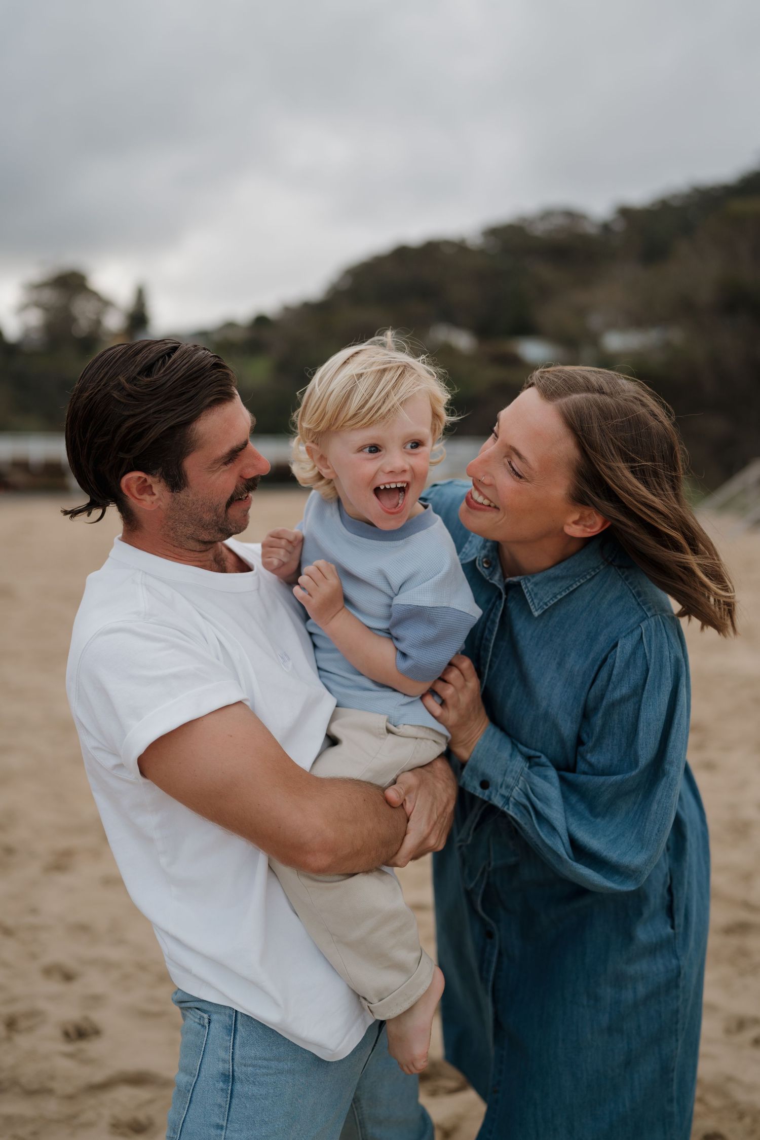 Joyful family moment captured on the beach with laughing toddler and parents.
