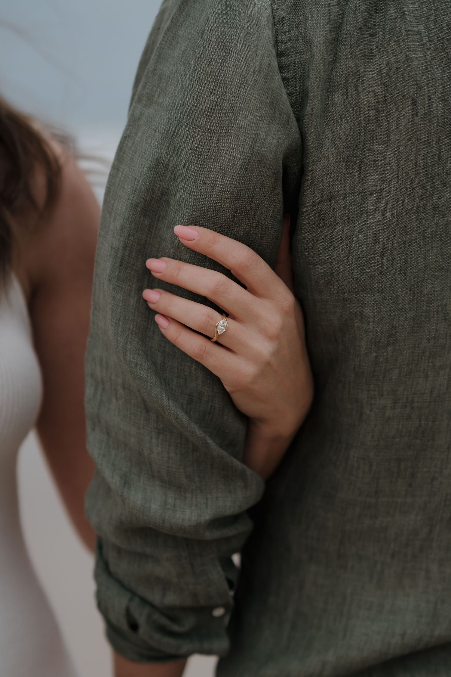 Close up detail of an engagement ring on hand against green fabric.