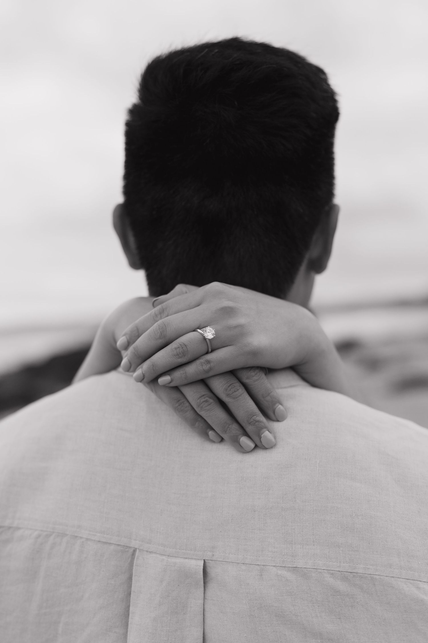 Close-up of hands gently resting on shoulders showing an engagement ring.