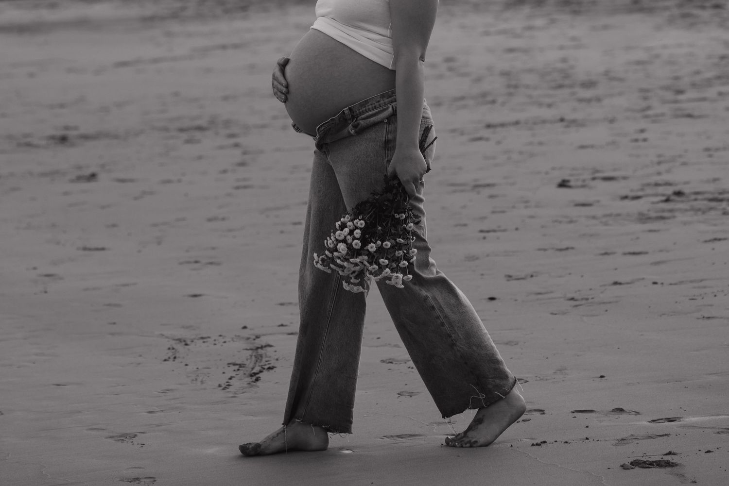 Silhouette of a pregnant woman walking on a beach in black and white.