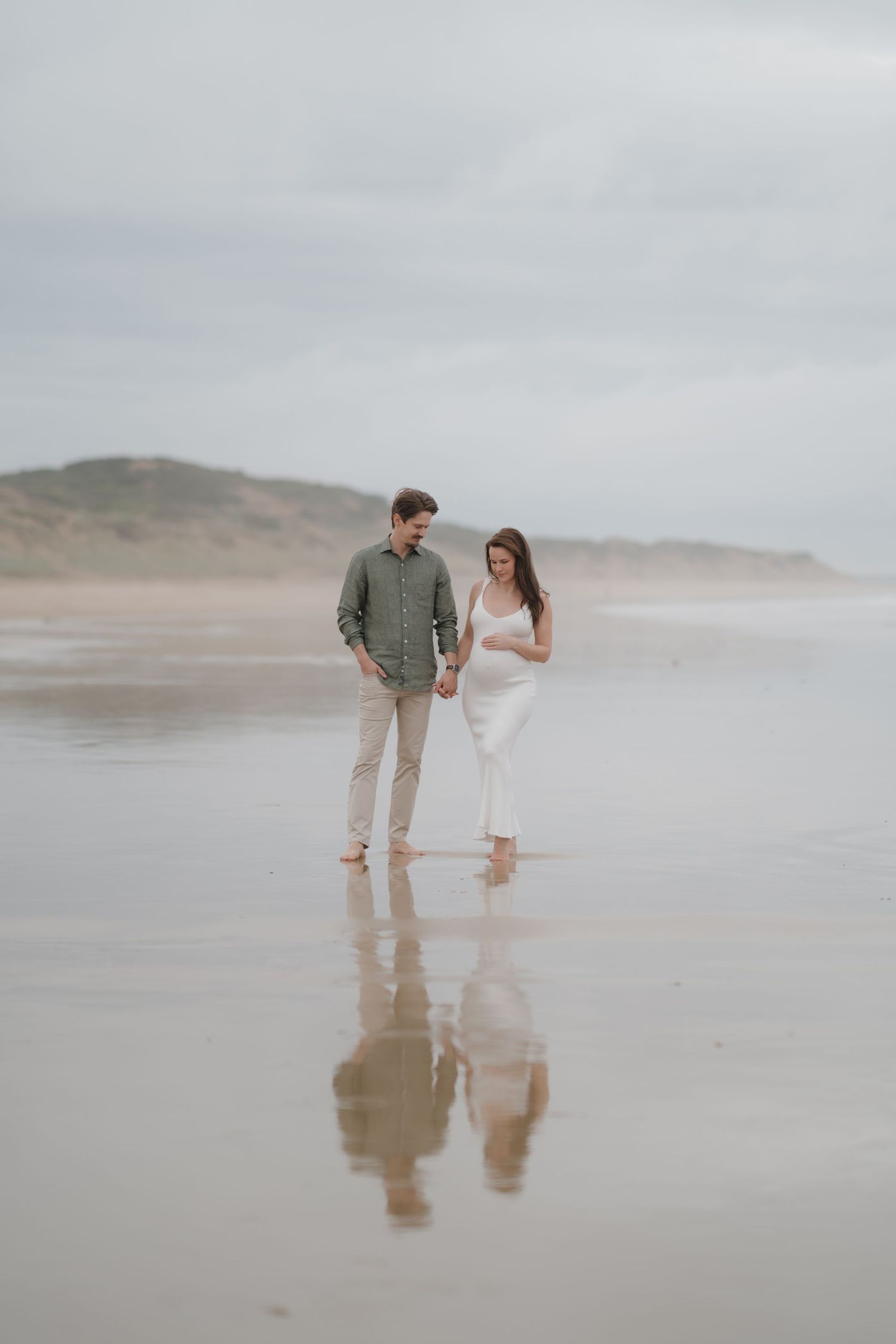 Couple walking together on misty beach with reflections in wet sand.