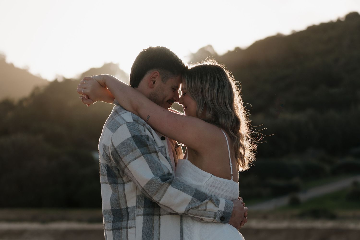 Intimate sunset engagement photo with couple embracing against mountain backdrop.