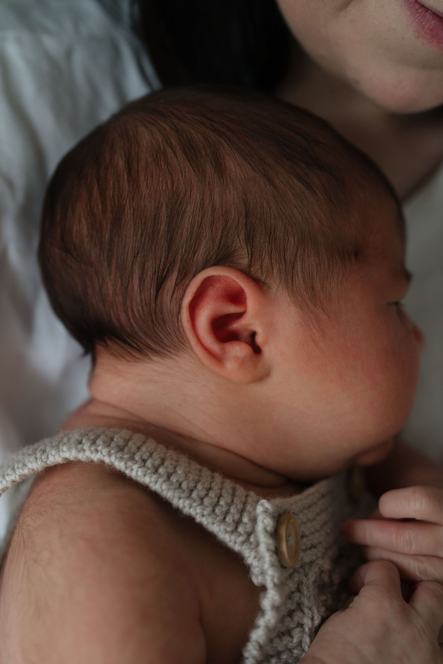 Close-up of a sleeping baby wearing a knitted cream-colored romper resting against soft white bedding.