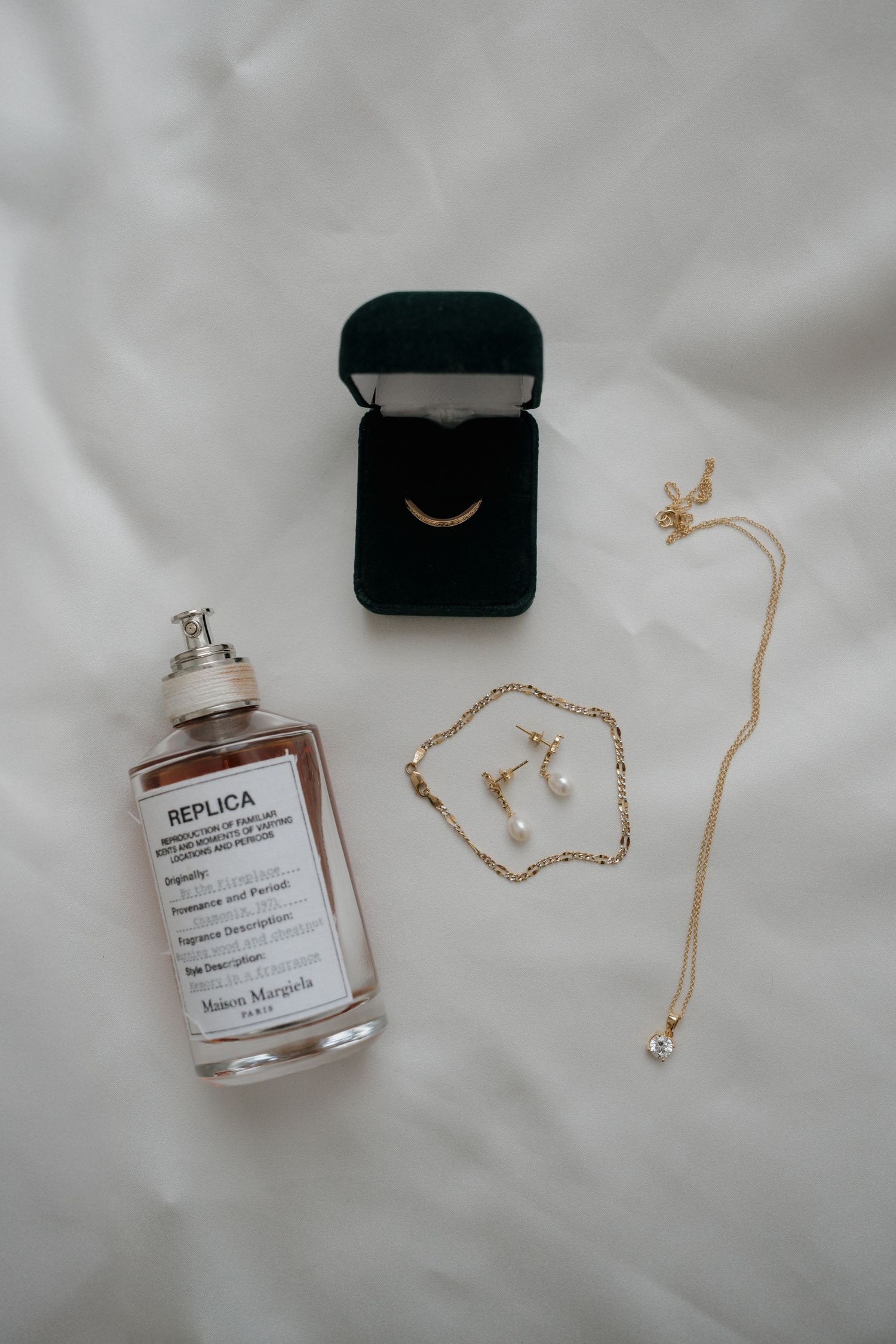 Wedding accessories including perfume bottle, jewelry, and ring boxes arranged on white surface.