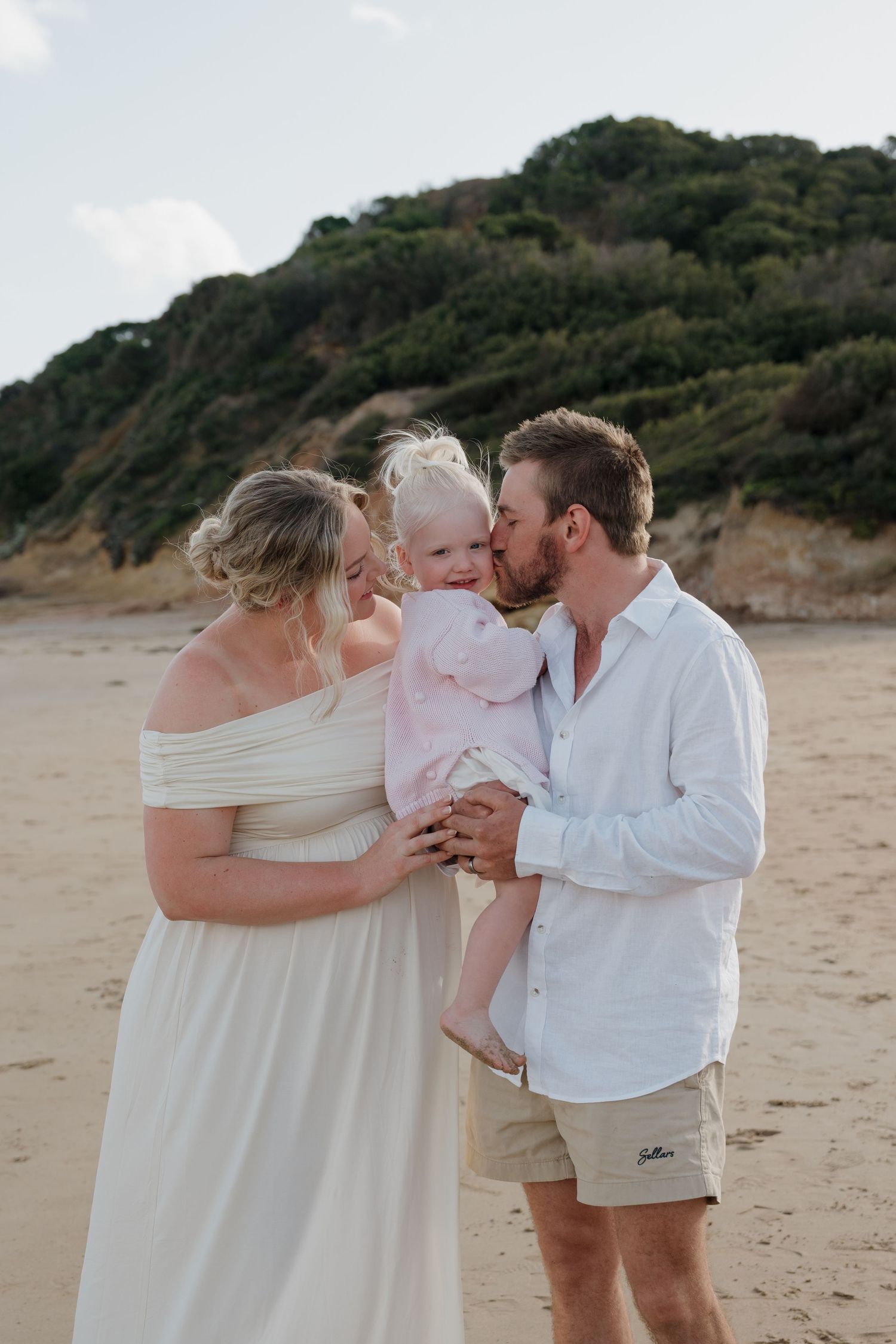 Family sharing an intimate moment on a beach with cliffs in the background.