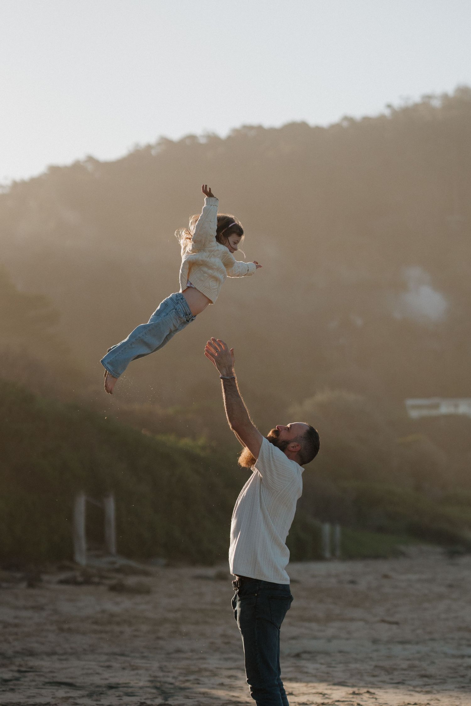 Father tossing child in air against sunset backdrop at beach.